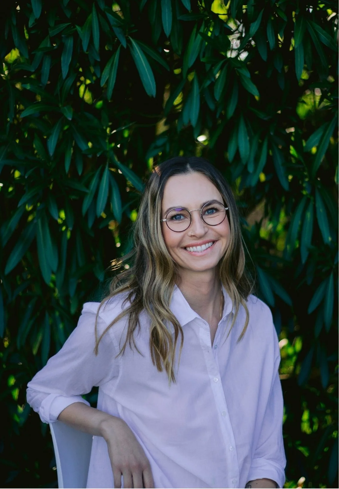 Adela Stone, a couples therapist, smiling in front of lush green foliage.