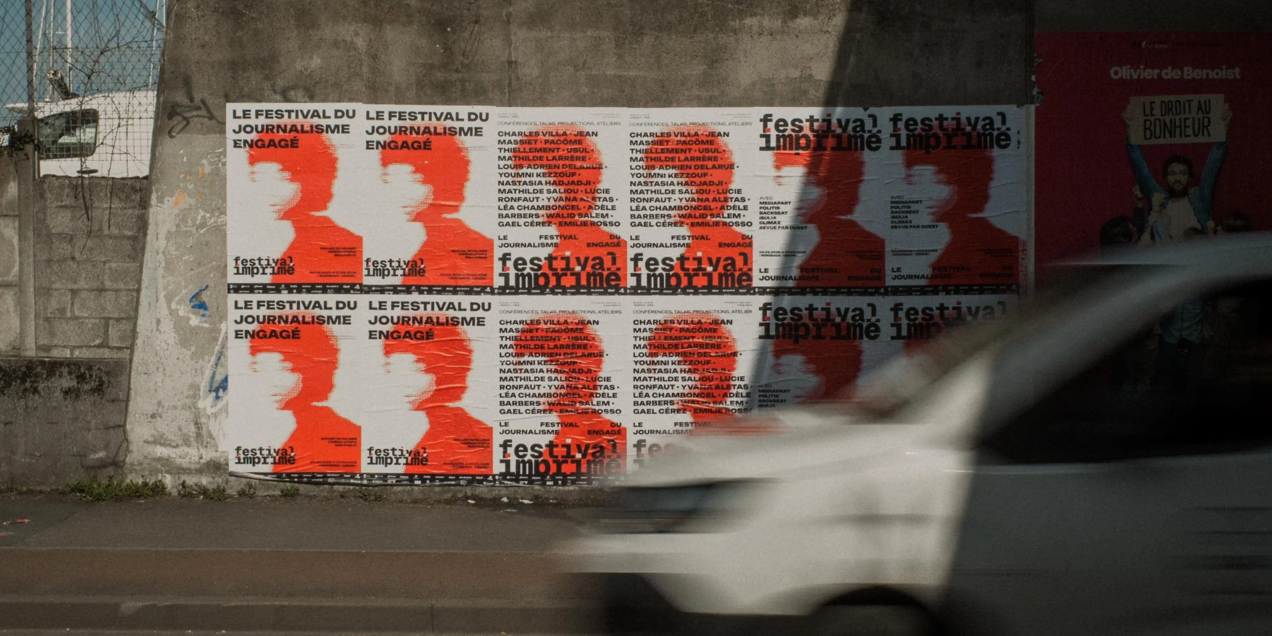 Affiches promotionnelles pour le festival du journalisme engagé, affichées sur un mur en béton, avec un véhicule en mouvement devant.