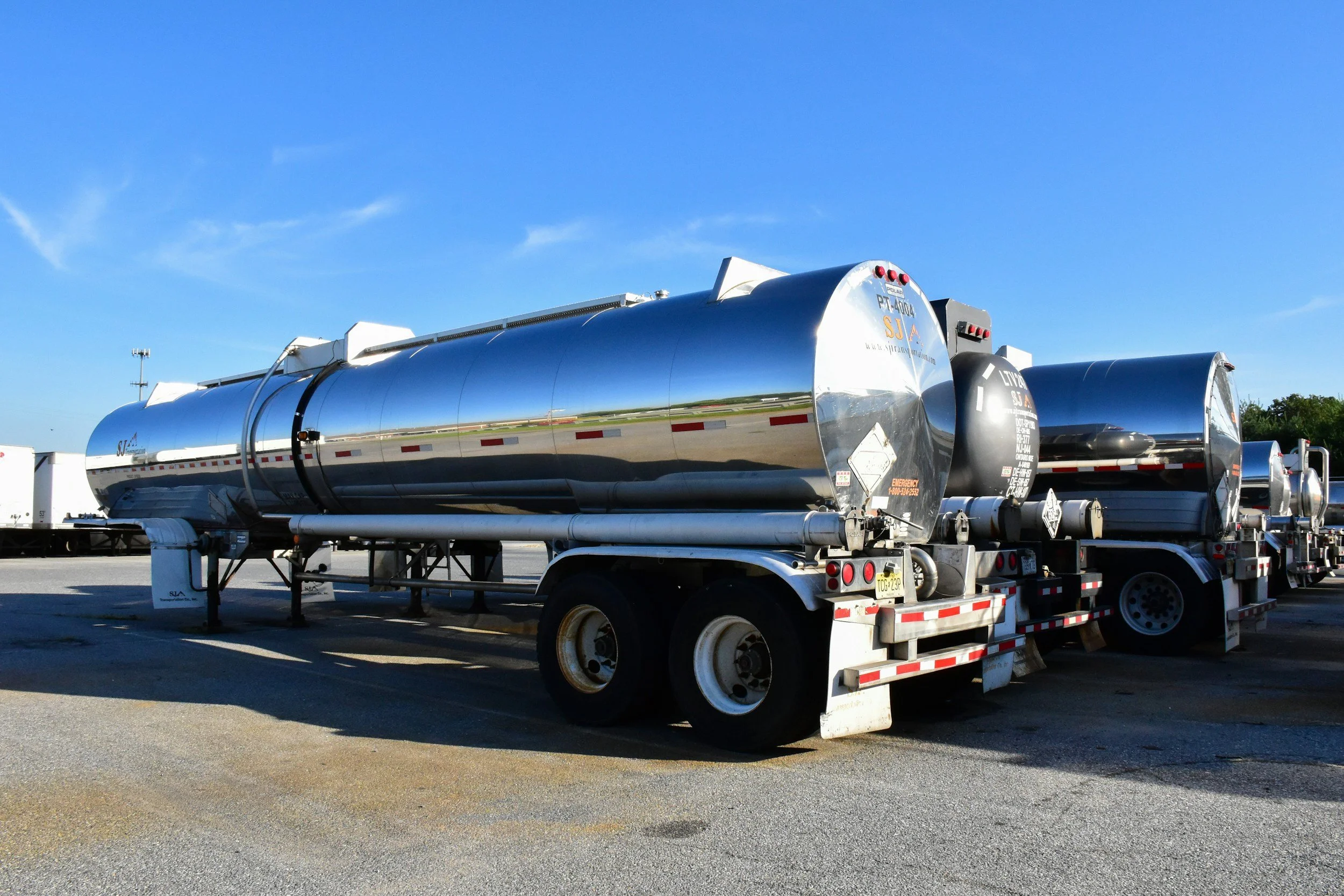 A shiny metal tanker truck parked on a lot with clear blue sky in the background.