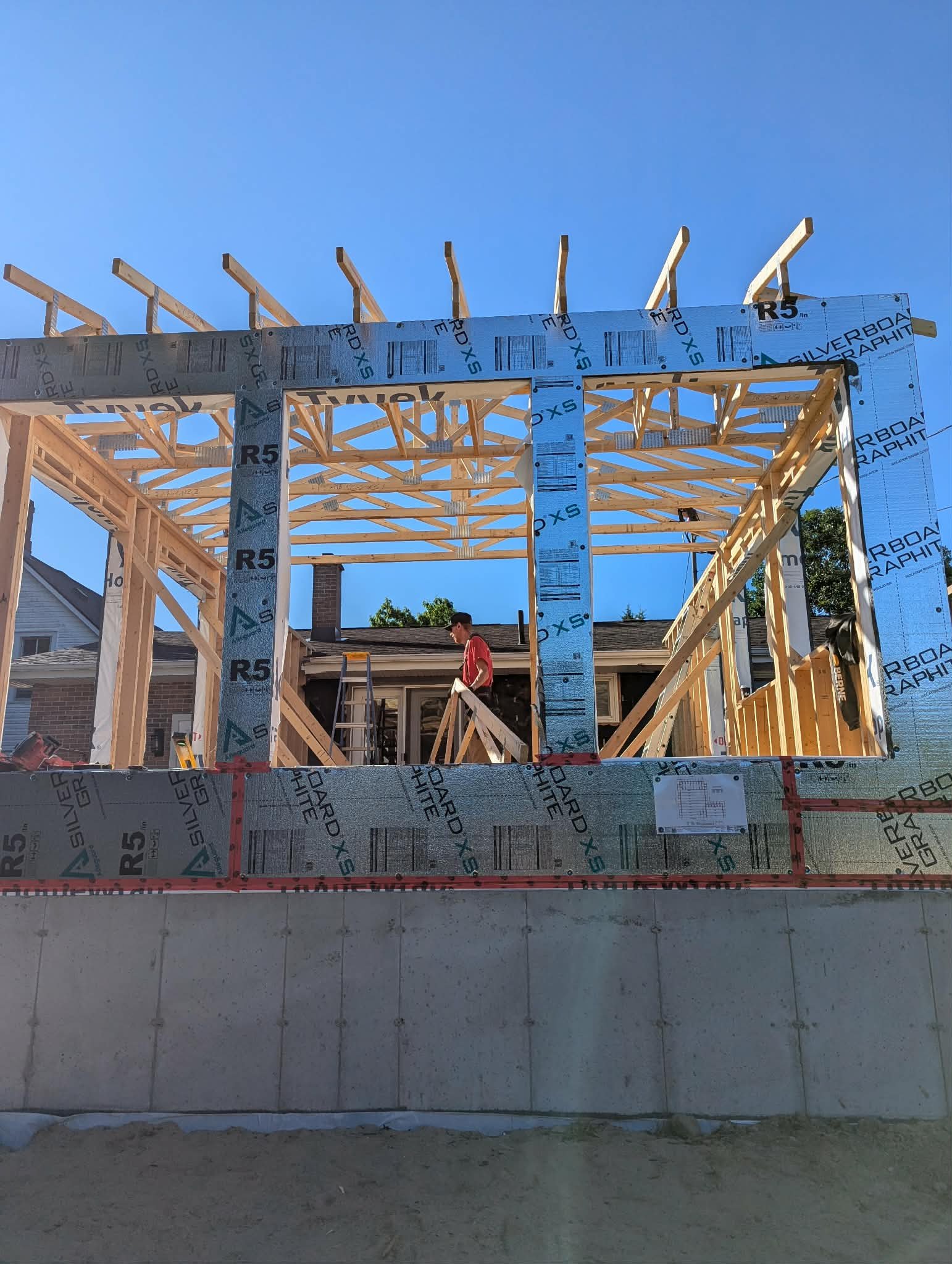 Construction worker building a house, wooden framework and roof trusses in progress against a blue sky.
