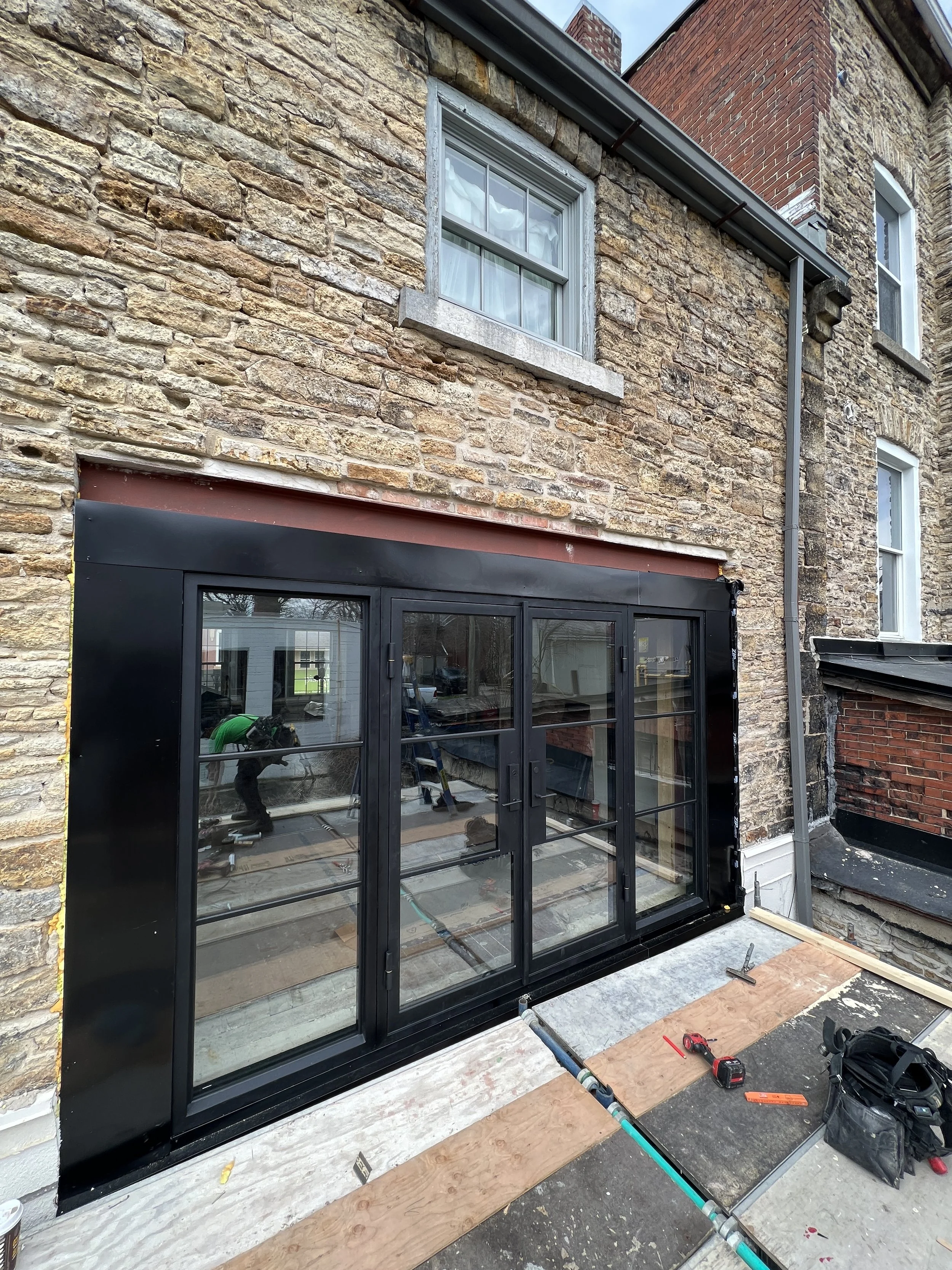 Construction workers install black-framed glass patio doors on a brick residential building exterior.