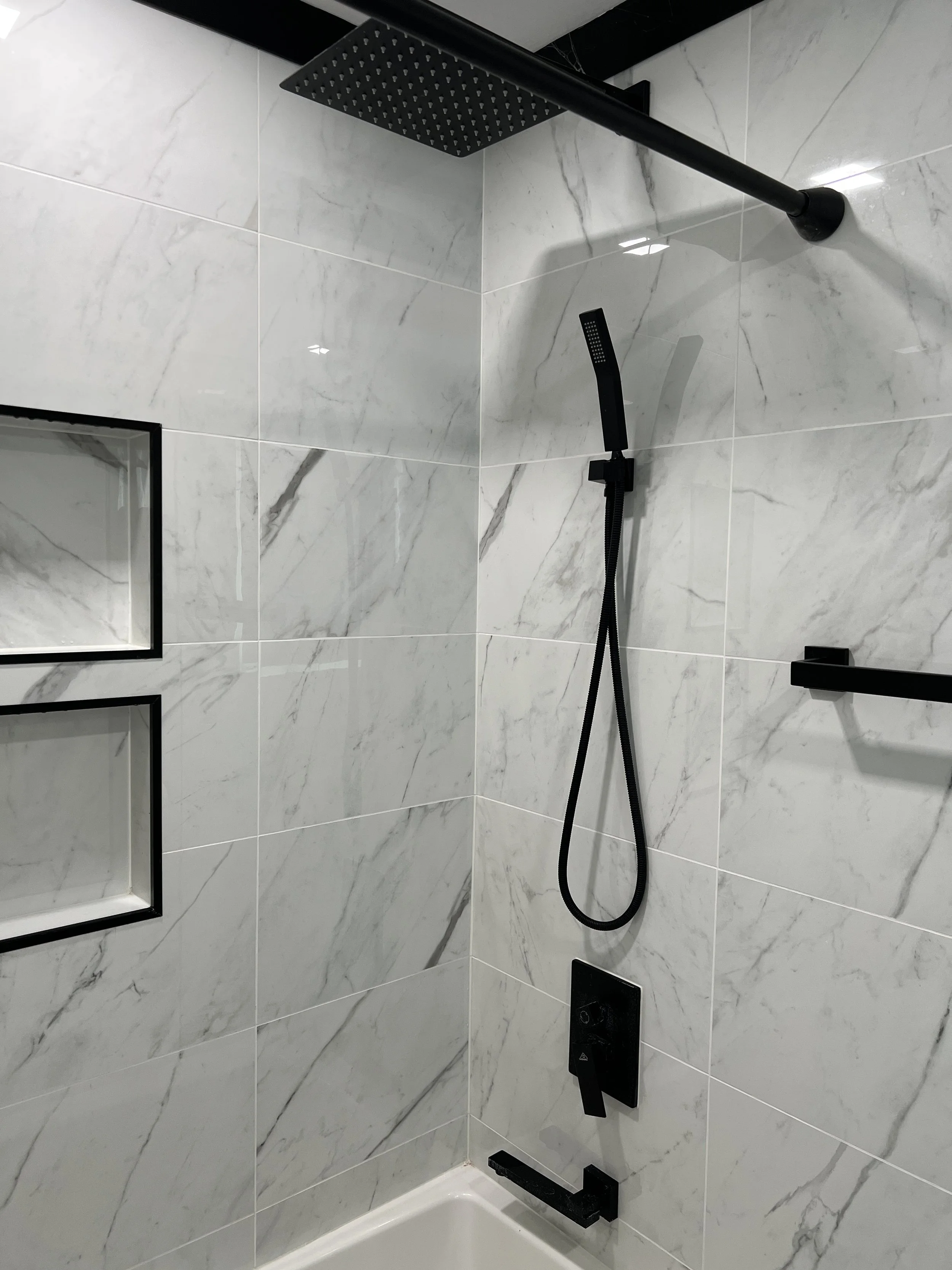 Modern shower with black fixtures, including a rainfall showerhead, a handheld showerhead, and a control panel on white marble tiled wall.