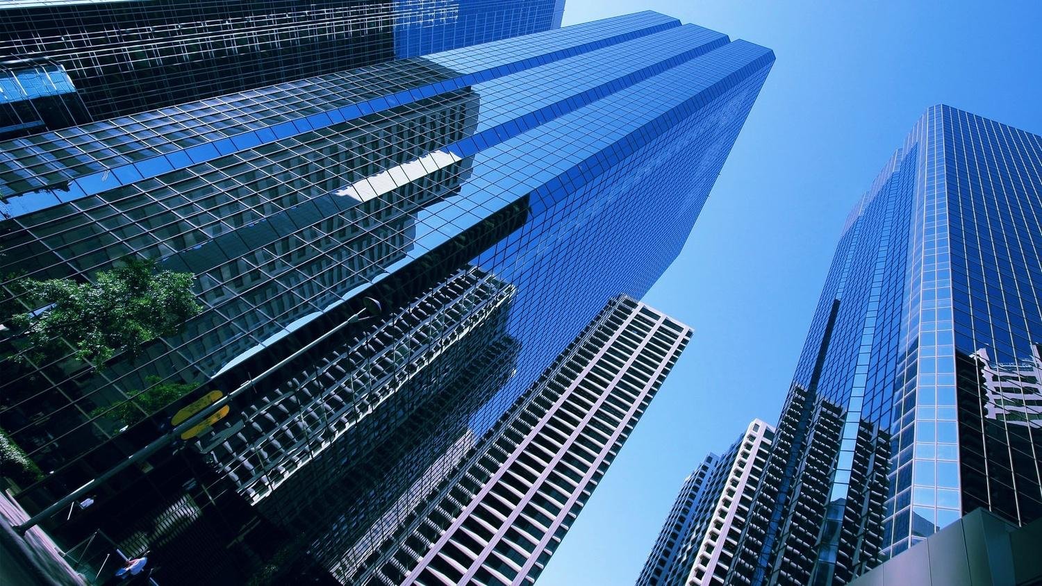 Perspective view of tall modern skyscrapers with glass facades reflecting sunlight against a clear blue sky.