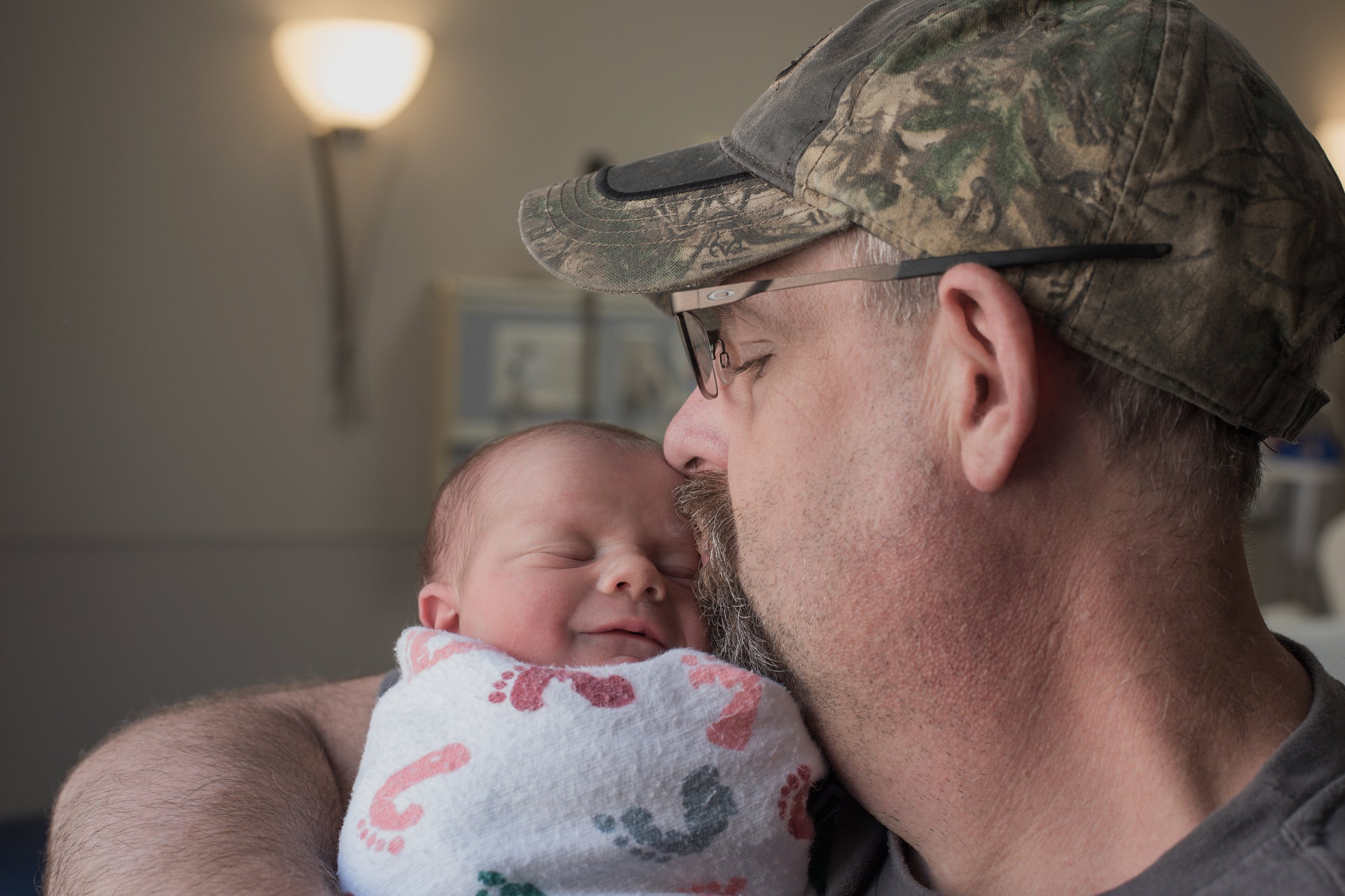 Fresh 48: Dad kissing newborn's head, baby smiling, moments made