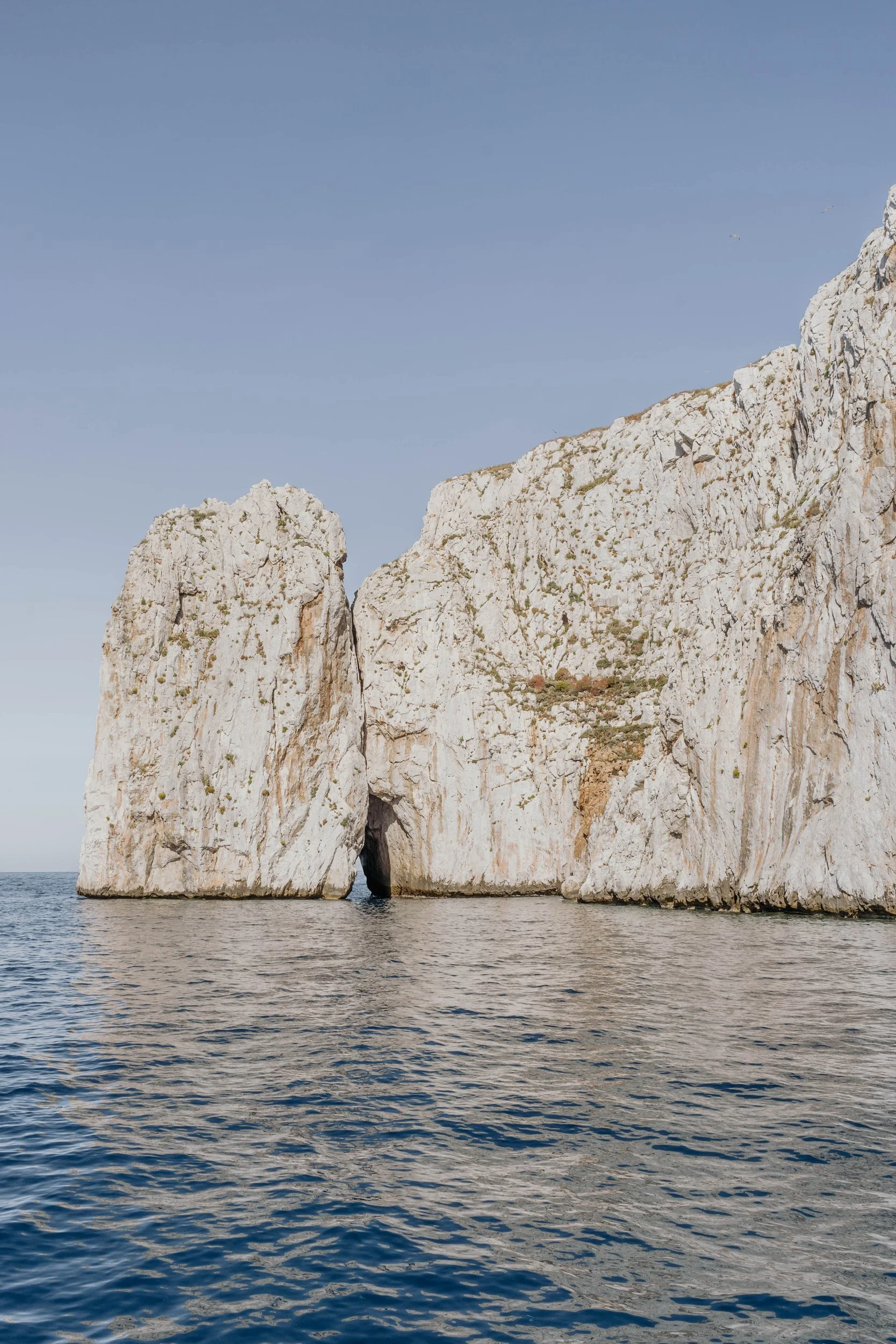 Pan di Zucchero, in Sardinia, surrounded by water with a clear blue sky above.