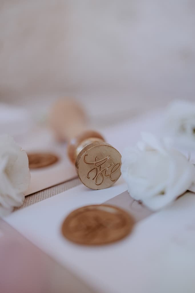 Wax seal stamp with the initials 'H' and 'C', surrounded by white roses and wax seals on a soft surface.