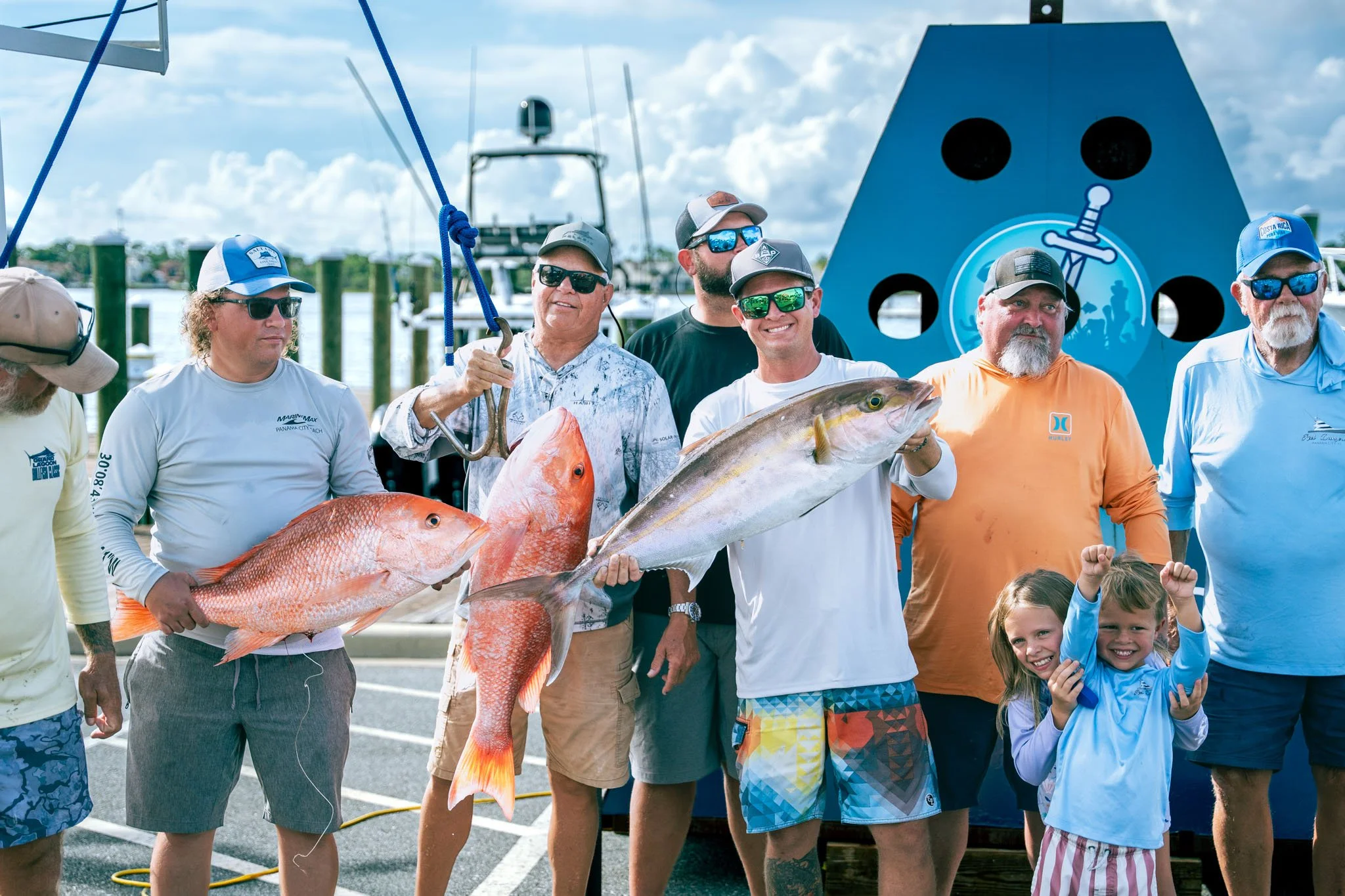 Group of people at Point South Marina - Bay Point (Panama City Beach) holding large fish, some smiling and wearing sunglasses and hats.