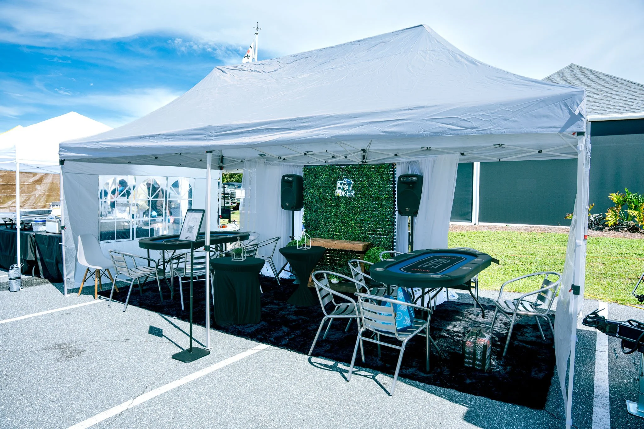 Outdoor event tent setup at Point South Marina - Bay Point (Panama City Beach) with tables, chairs, a poker sign, and a decorative green wall, under a sunny sky.
