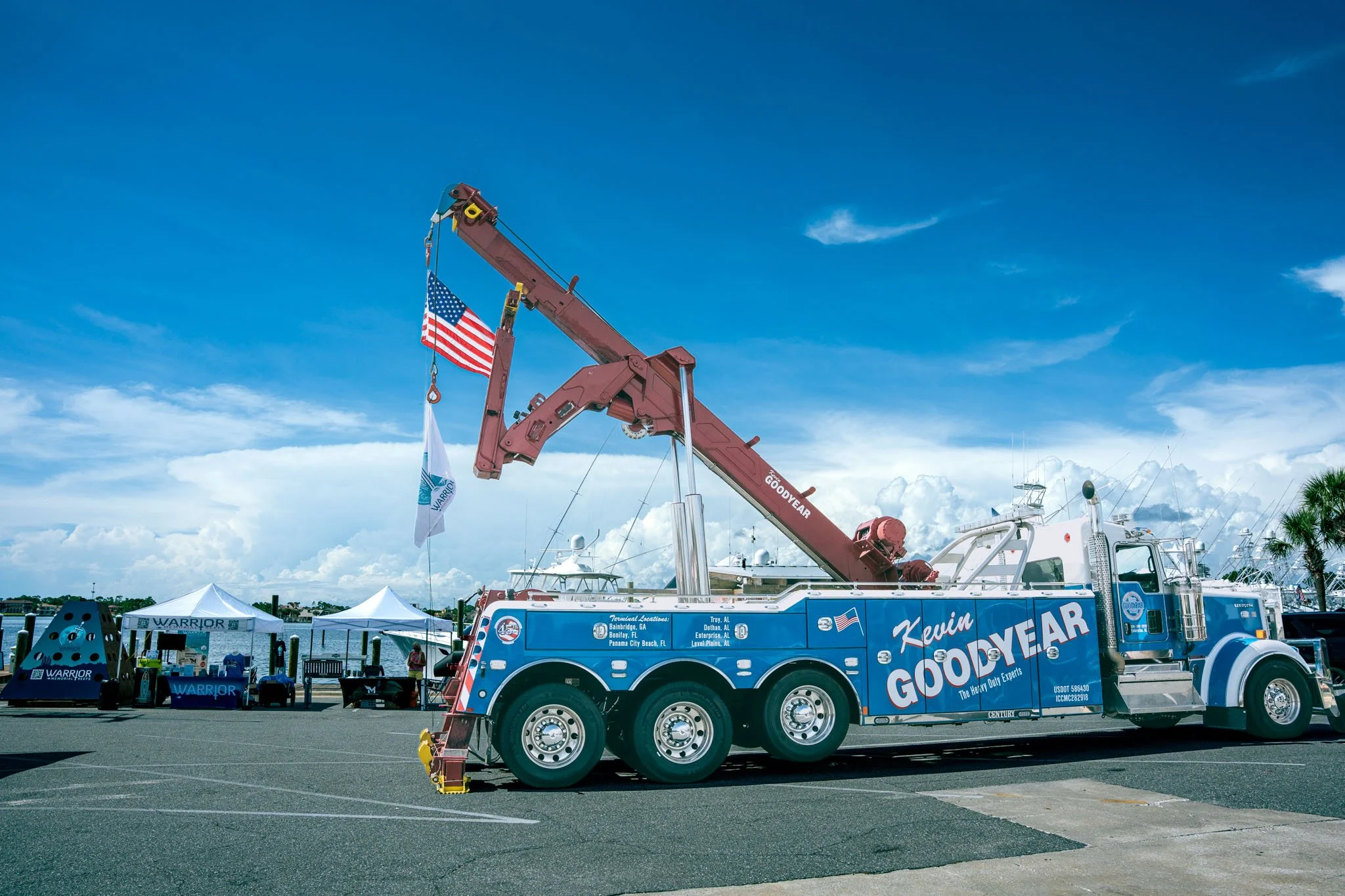 A tow truck with Kevin Goodyear branding and American flags stationed at Point South Marina - Bay Point (Panama City Beach) with boats and tents.