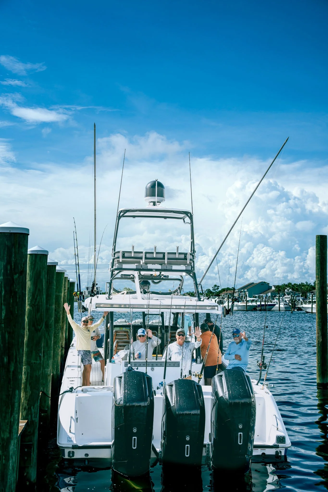 People on a boat docked at Point South Marina - Bay Point (Panama City Beach), waving and enjoying a sunny day, with blue sky and white clouds in the background.