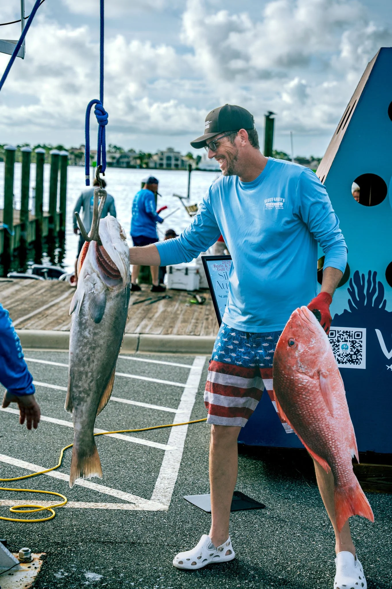 Man holding large fish at the Warrior Memorial Reefs Reels and Spears Fishing Tournament event at Point South Marina - Bay Point (Panama City Beach), multiple people and water in background