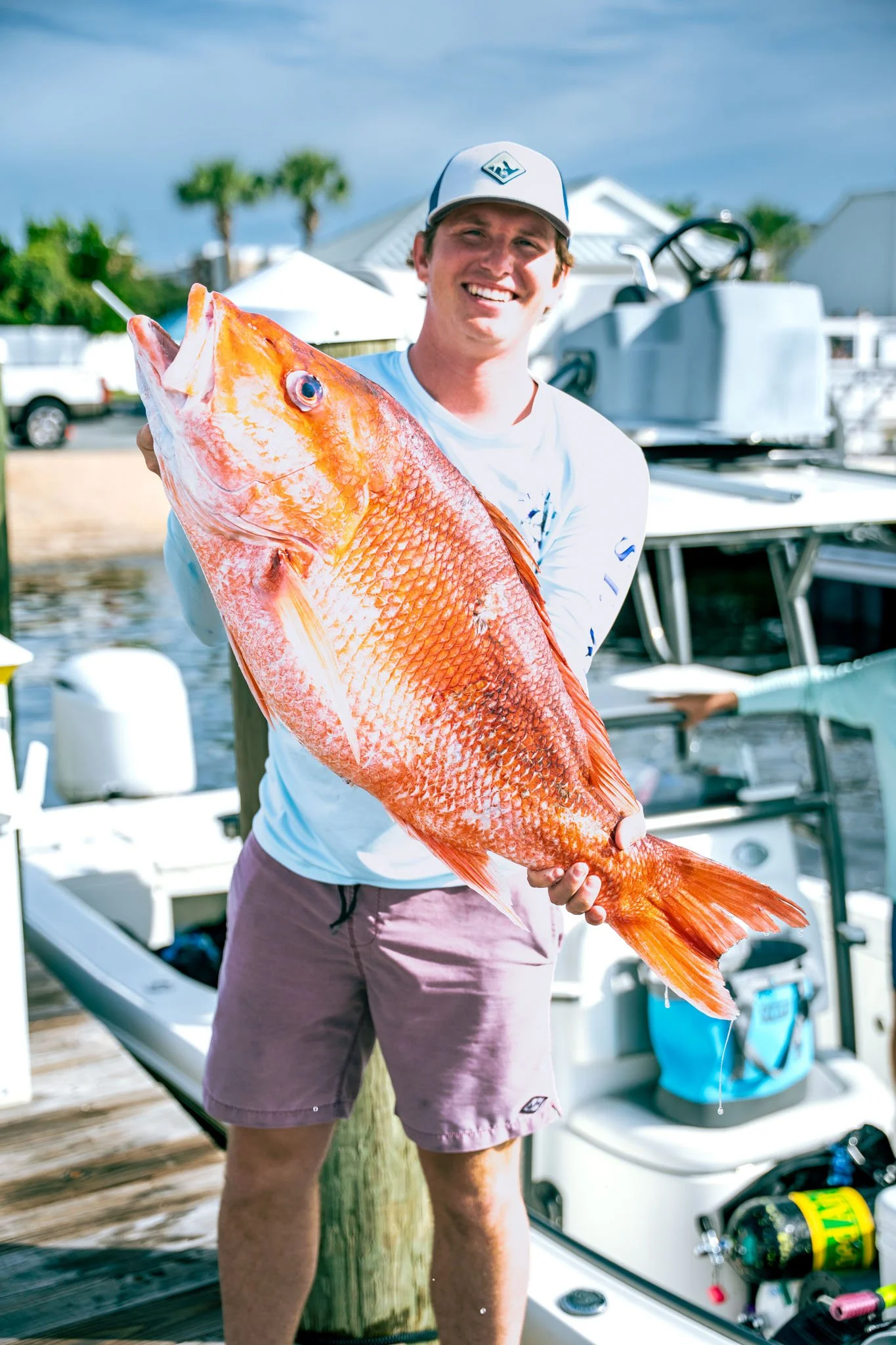 A man holding a large orange fish on a dock at Point South Marina - Bay Point (Panama City Beach) near boats and water.