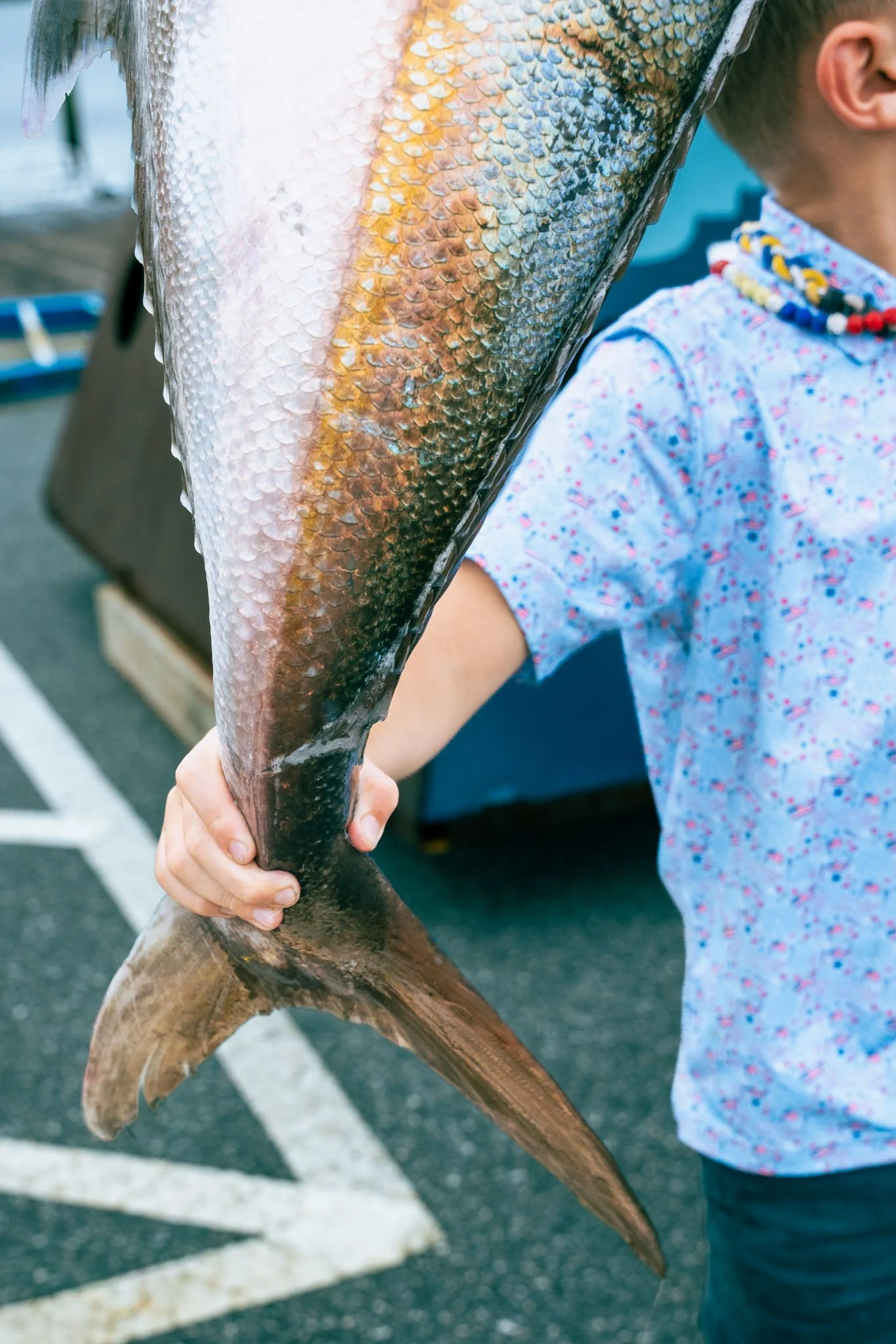 Child holding a large fish, likely at a fishing location or market.