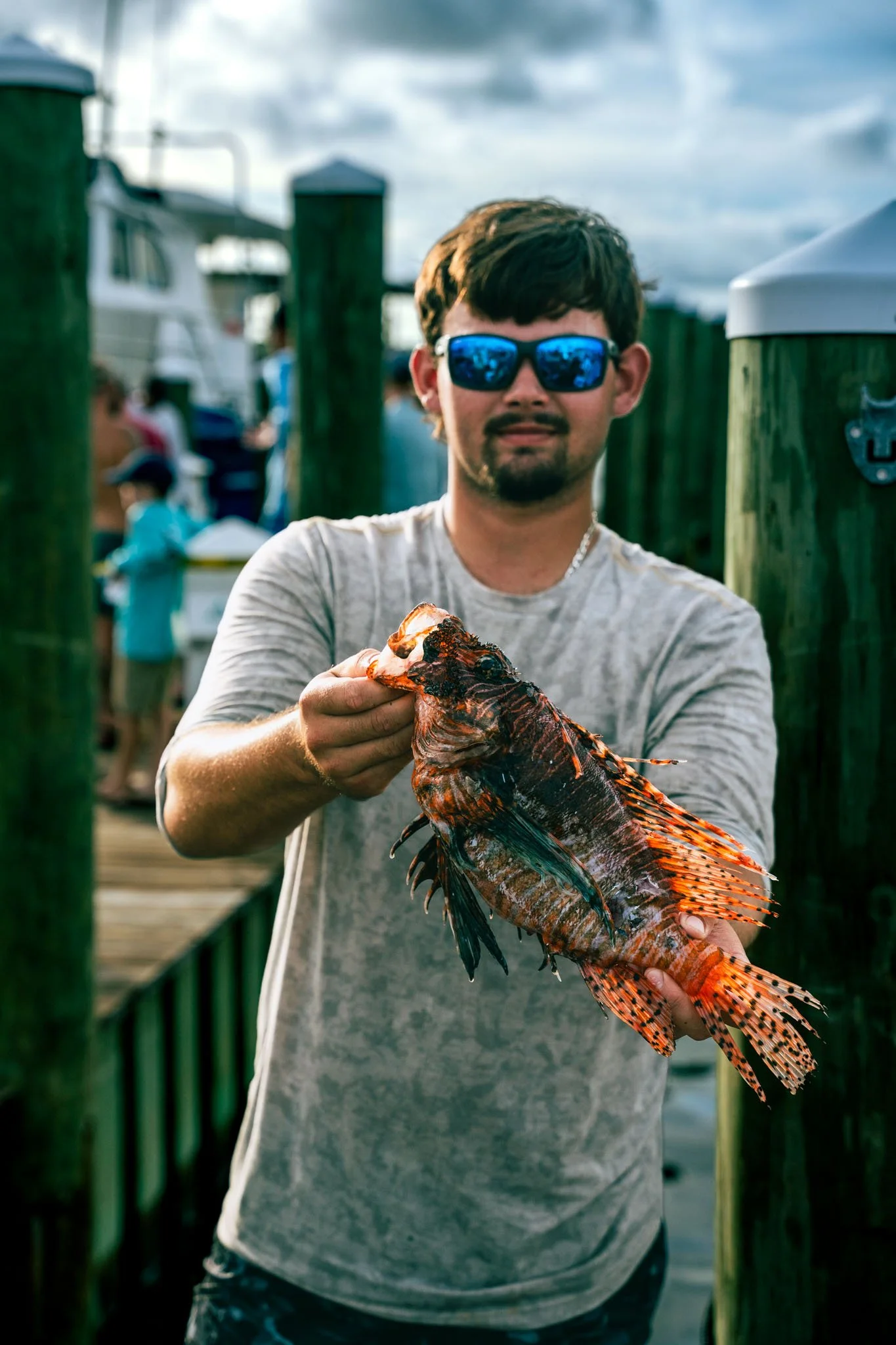 Man wearing sunglasses holding a large orange and black fish on a dock at the Warrior Memorial Reefs Reels and Spears Fishing Tournament event at Point South Marina - Bay Point (Panama City Beach).