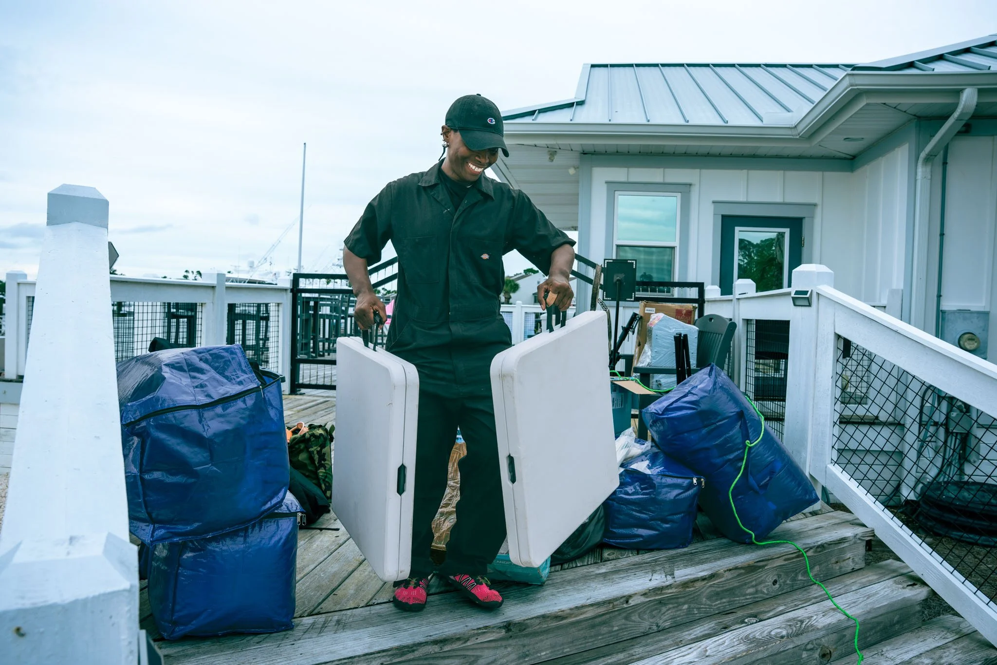 A woman smiling at Point South Marina - Bay Point (Panama City Beach) and organizing items on a porch, surrounded by blue bags and outdoor furniture.