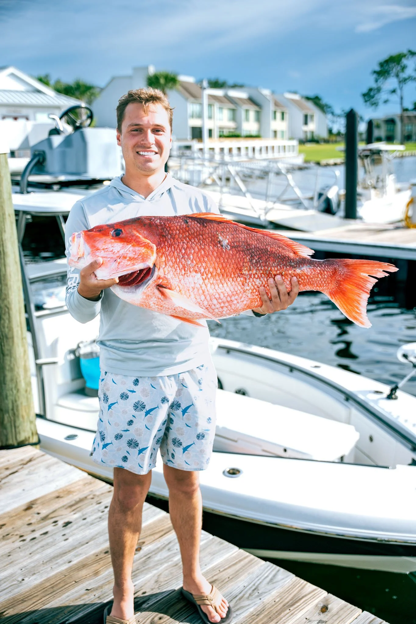 A man holding a large red fish on a dock at Point South Marina - Bay Point (Panama City Beach) near boats and water.