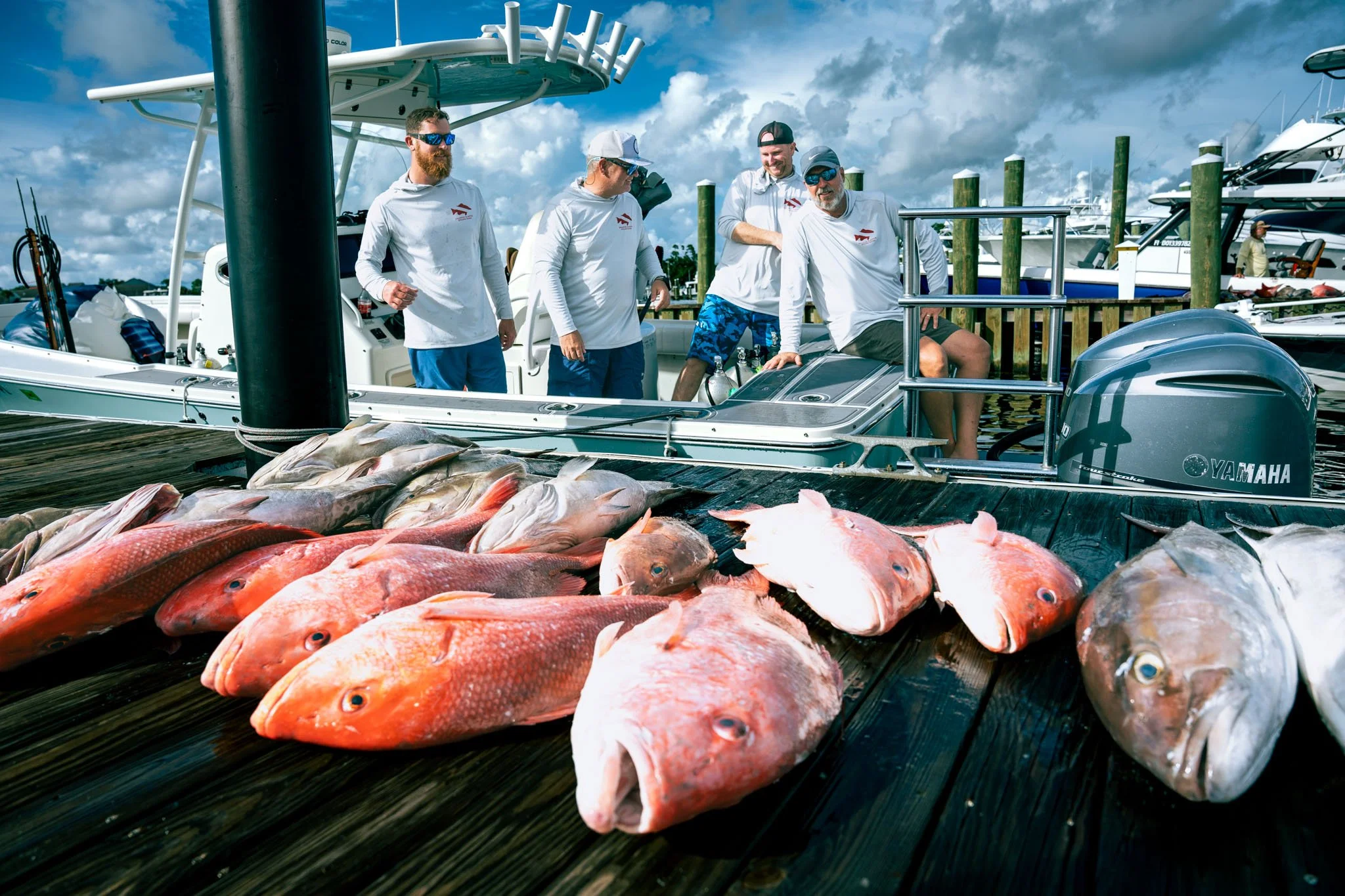 A group of people on a boat at Point South Marina - Bay Point (Panama City Beach), with fish laid out on the dock in front of them, and other boats docked nearby.