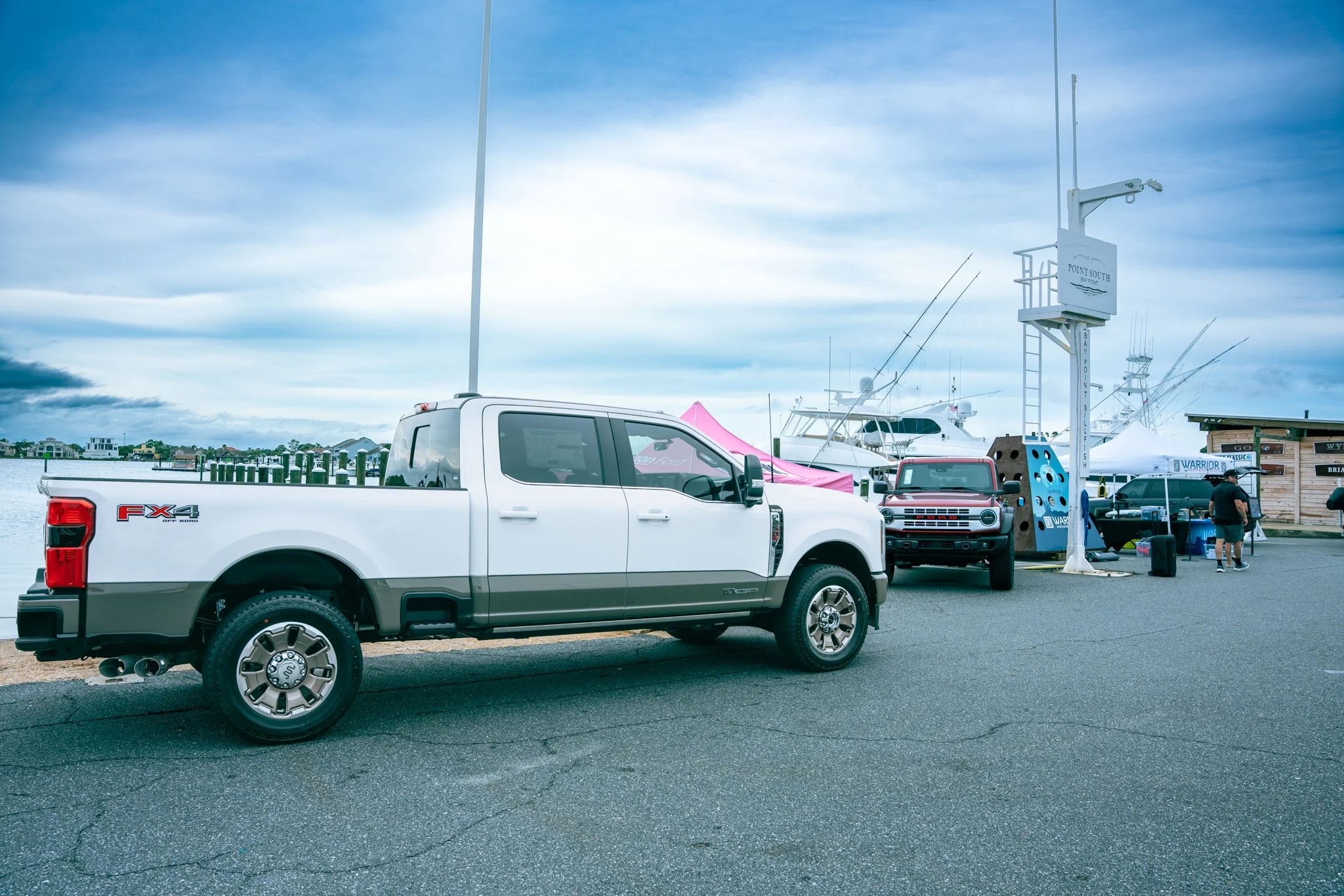 A white pickup truck parked at Point South Marina - Bay Point (Panama City Beach) with yachts in the background and a vibrant blue cloudy sky overhead.