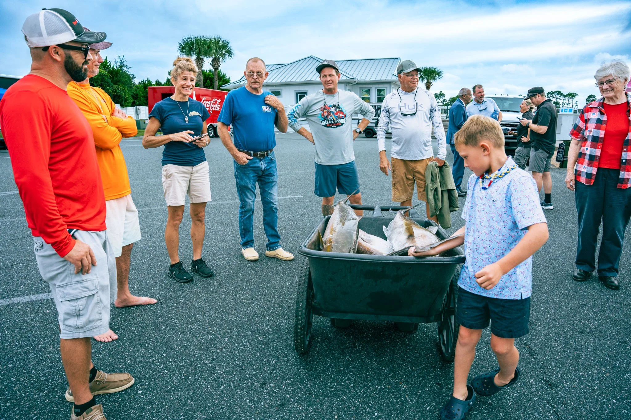 Group of people gathered outdoors near a building, with a cart of large fish in front of them.