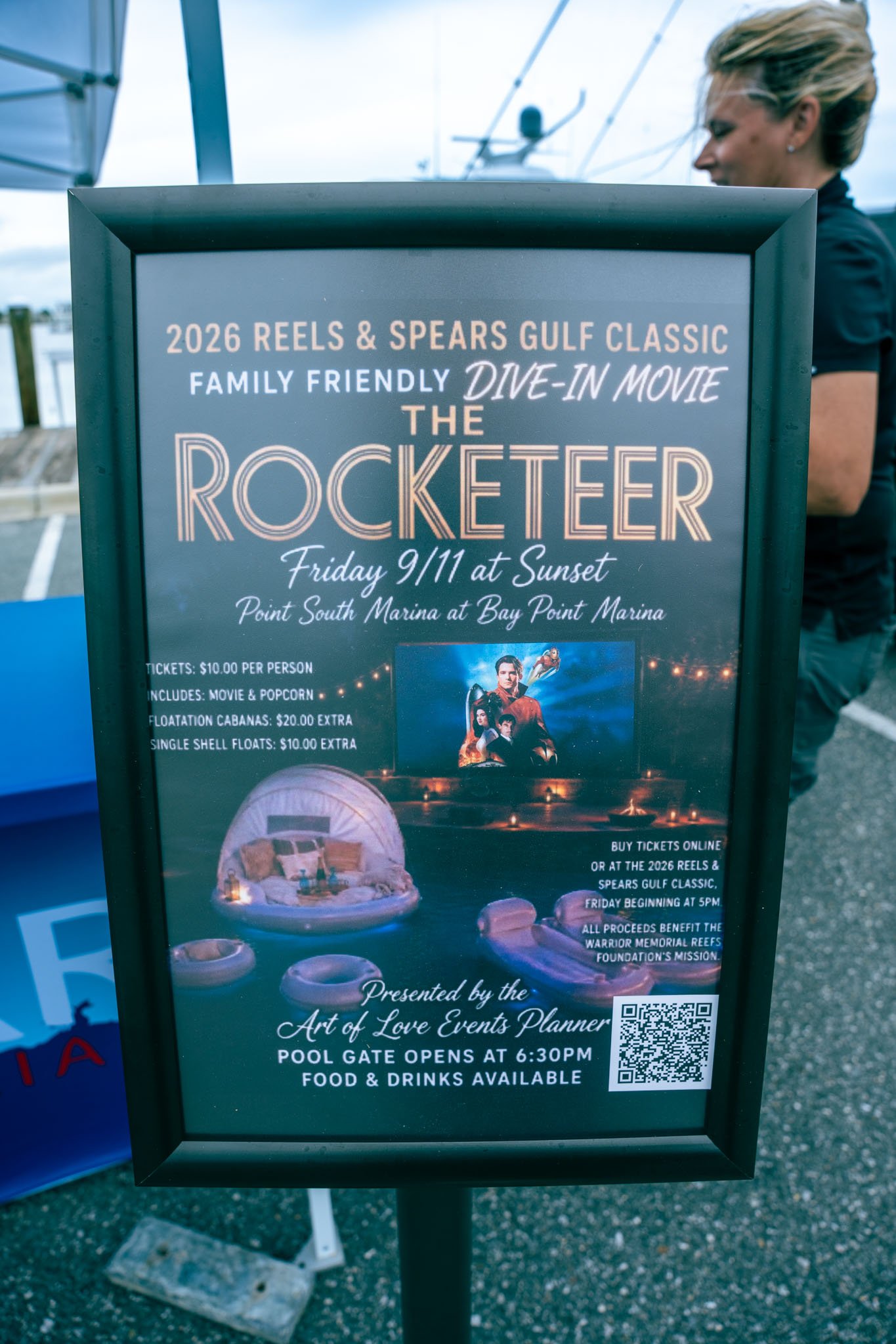 Promotional sign for 2026 Reels & Spears Gulf Classic family-friendly dive-in movie event, featuring The Rocketeer, at sunset on Friday, September 11th at Point South Marina, Bay Point Marina. Ticket info, event details, and a QR code are included.
