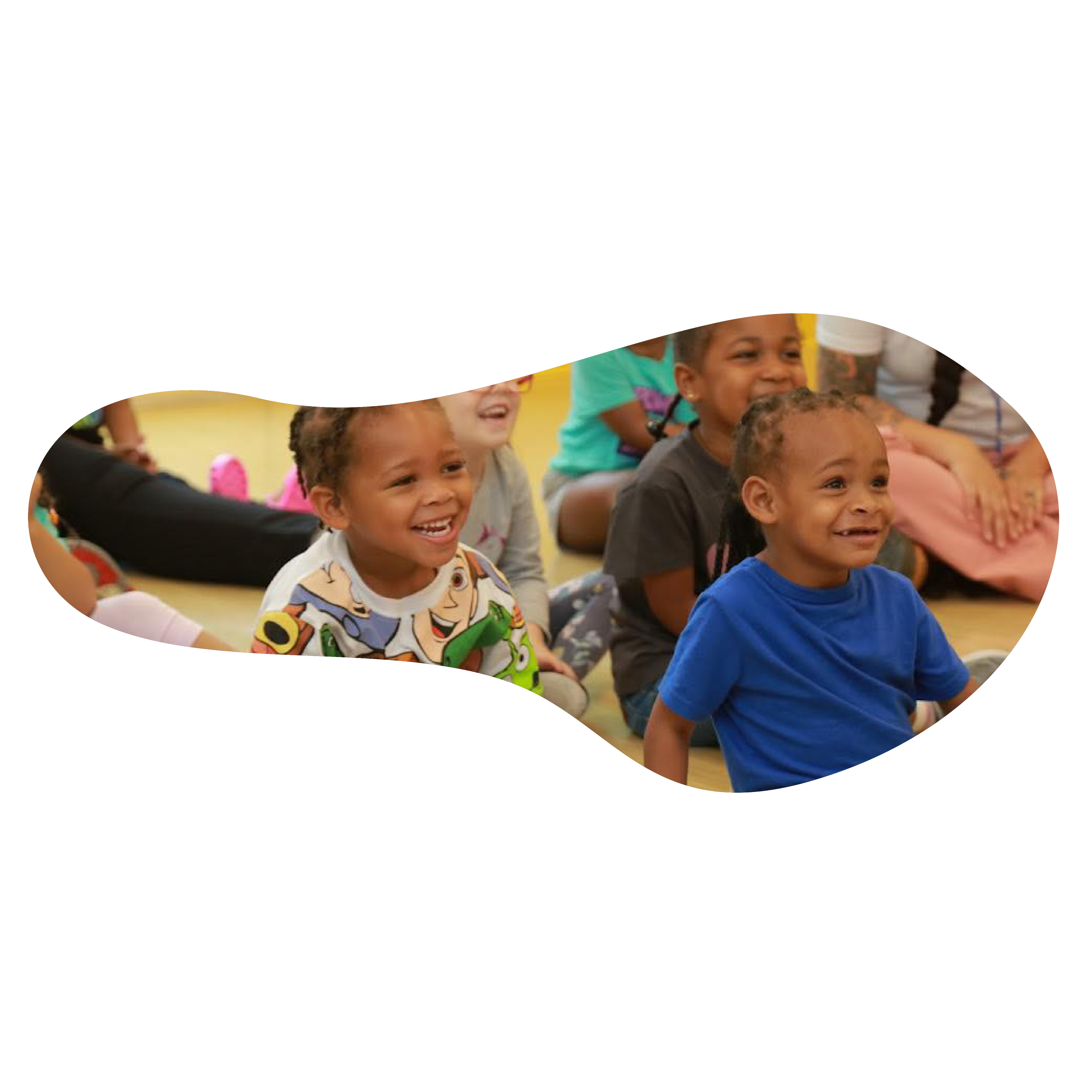 Group of young children sitting on the floor, smiling and laughing during an activity in a classroom or daycare setting.