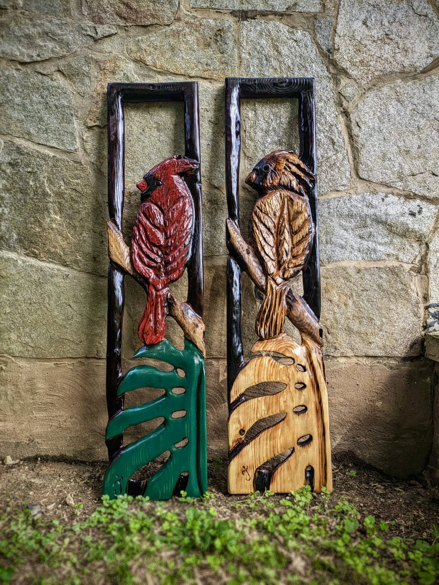 Colorful wooden wall art of two tropical birds perched on leaves, mounted against a stone wall
