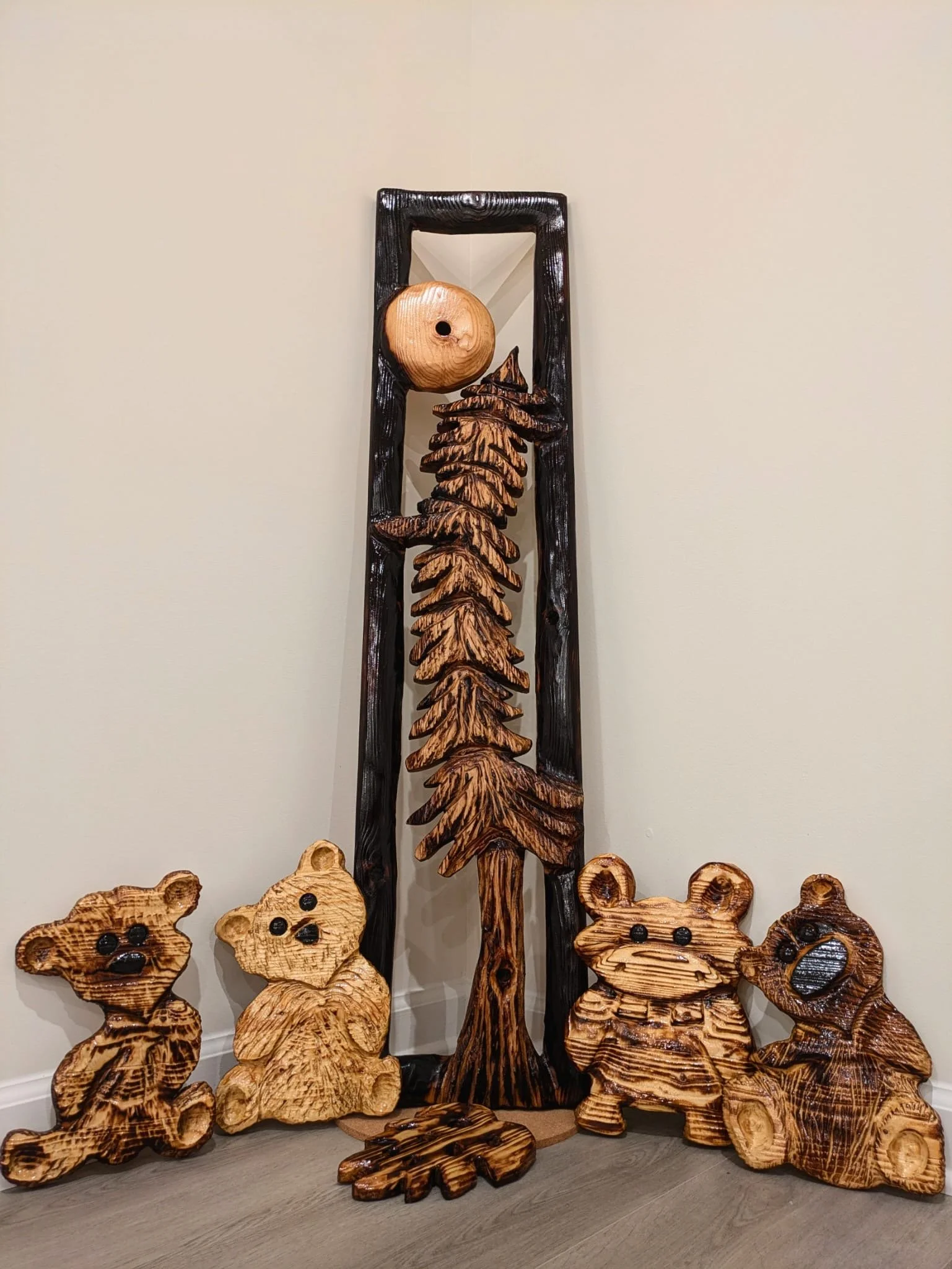Wooden bear, tree, leaves, and apple sculptures arranged indoors against a beige wall.