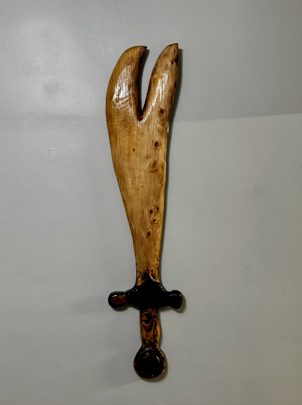 Decorative wall hanging in the shape of a knife, made from polished wood with a dark handle, mounted on a plain white wall.
