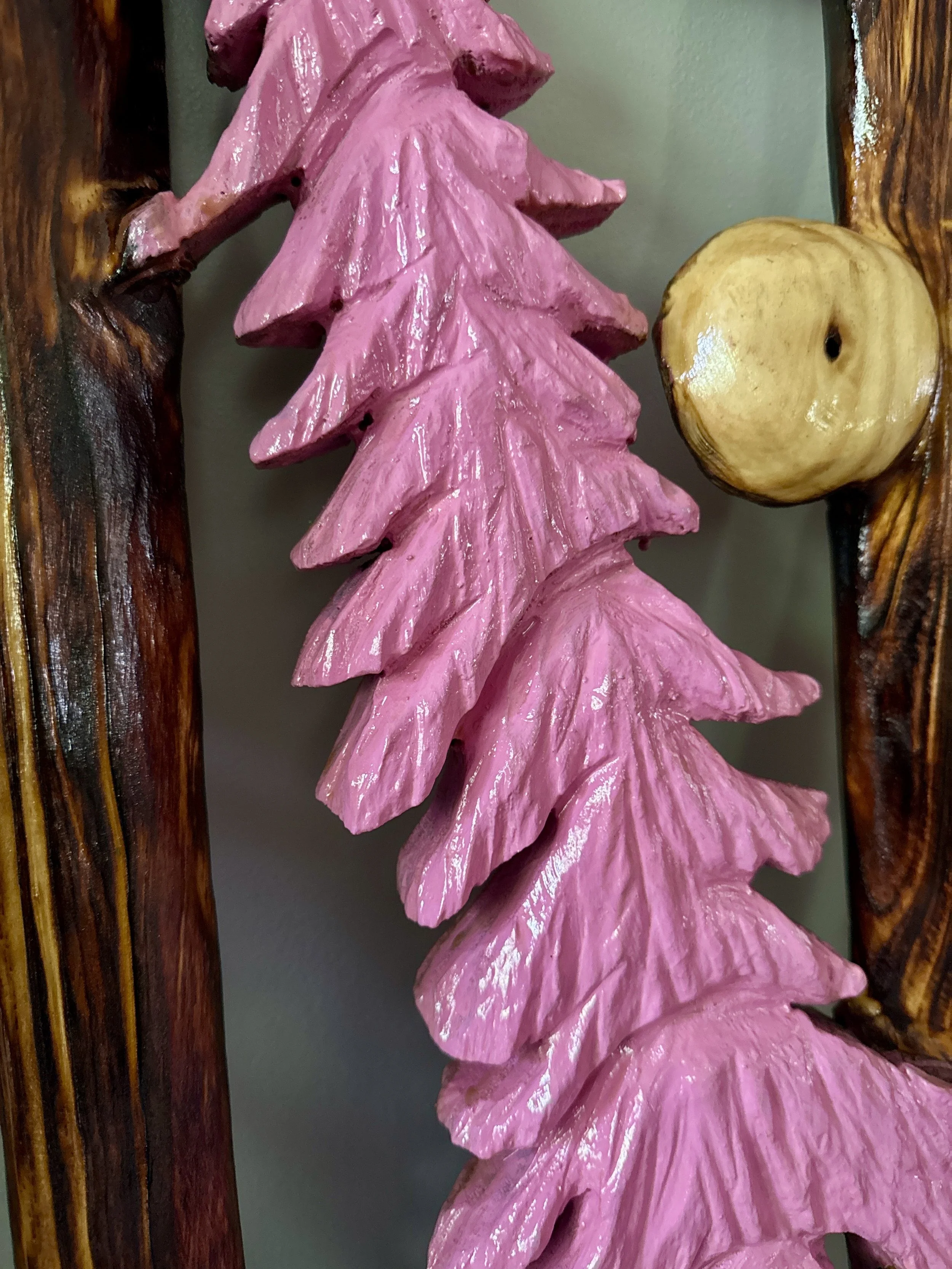 Close-up of a handcrafted wooden art piece featuring large, pink painted leaves with detailed vein patterns, attached to a frame made of polished wood with a light-colored round wooden element.