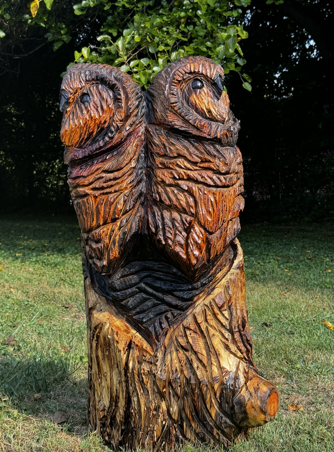 Wooden sculpture of a wolf in a grassy park with trees in the background.