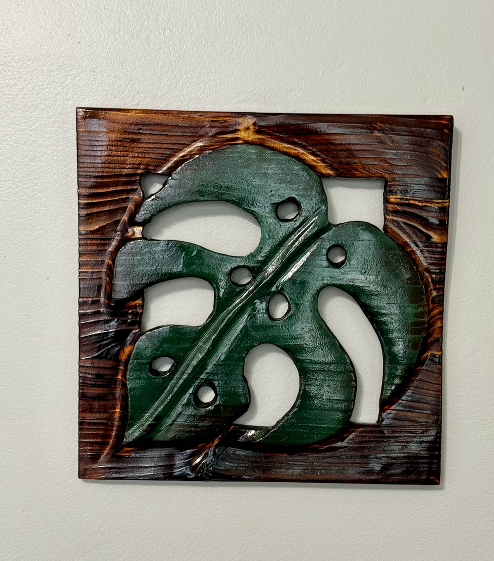 Wall decor featuring a carved wood leaf with a dark brown frame.