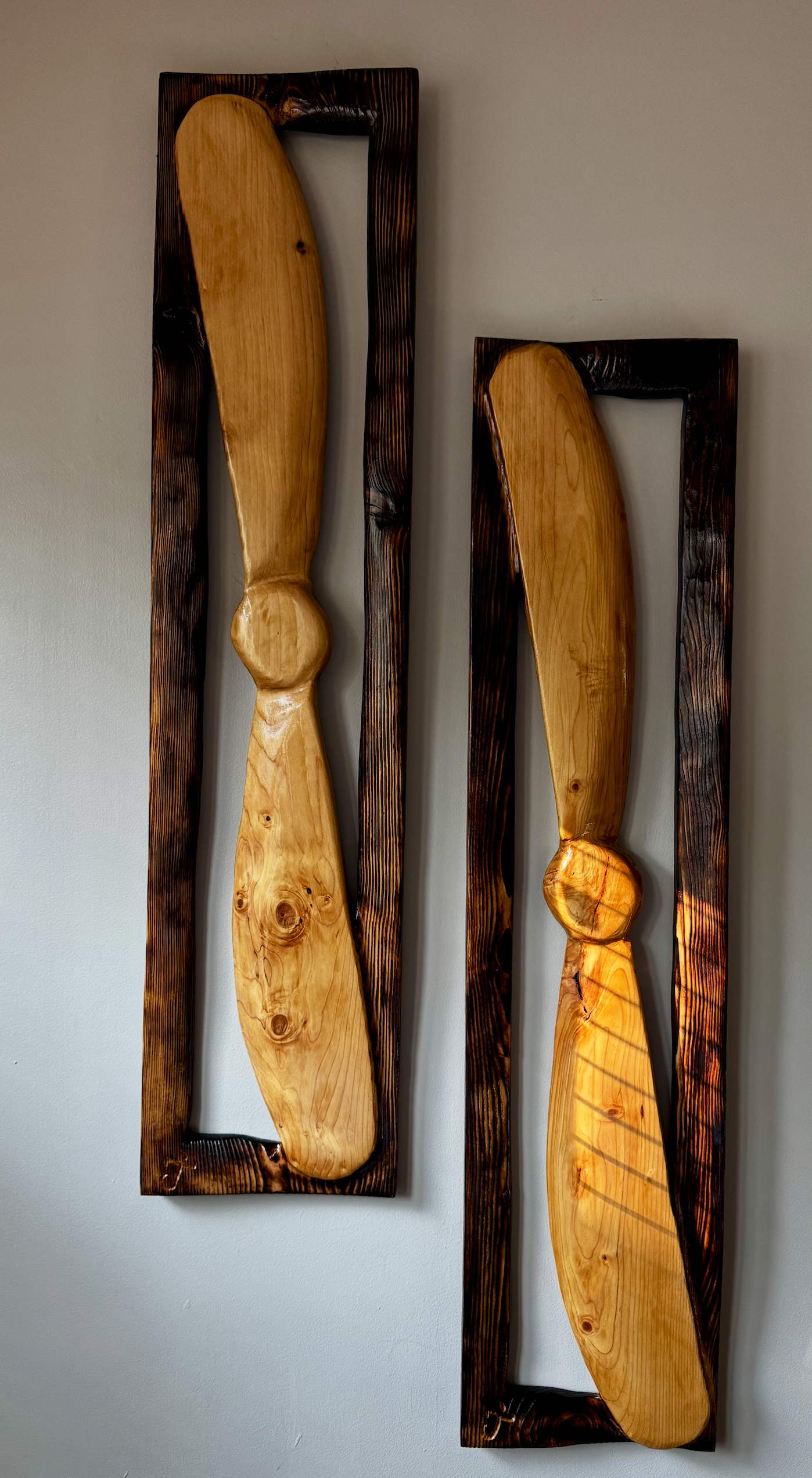 Wooden wall art with two large, curved, polished wooden spoons mounted on dark wooden frames with rectangular shapes.