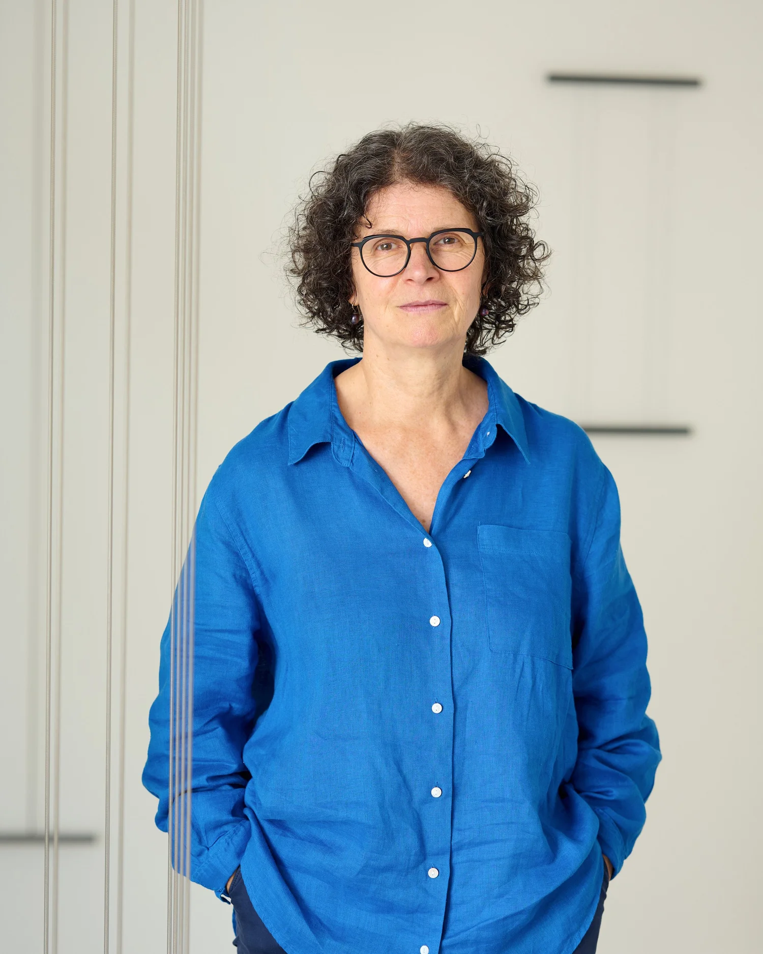 Elisabeth Heindl im blauen Hemd, stehend zwischen feinen vertikalen Linien ihrer Arbeit.