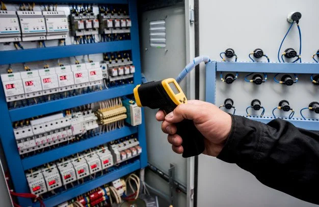 Person using a thermal infrared thermometer to check an electrical control panel with circuit breakers.
