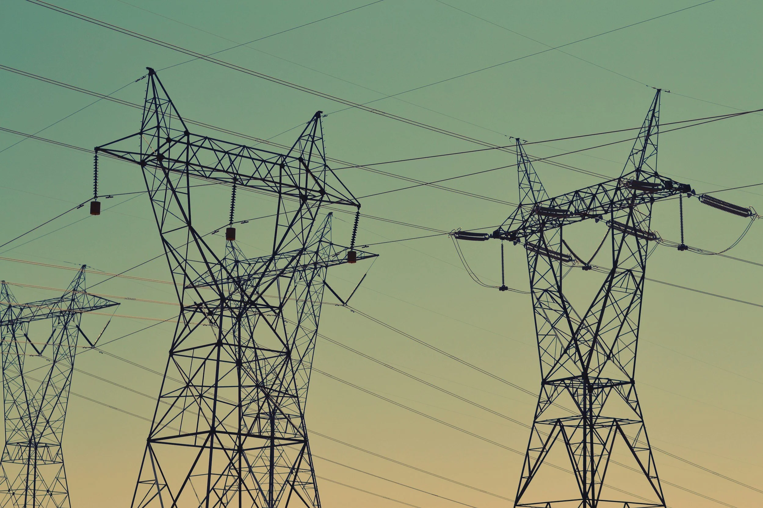 Silhouettes of electrical power transmission towers against a gradient sky.