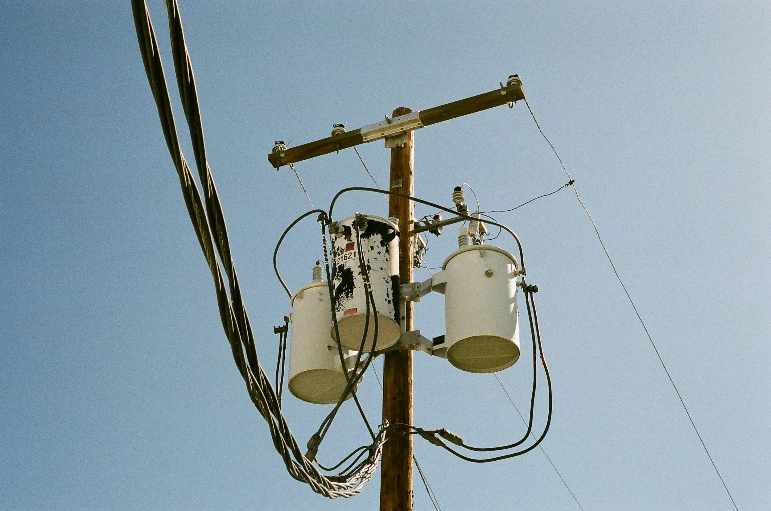 Electrical utility pole with transformers and wires against a clear blue sky.