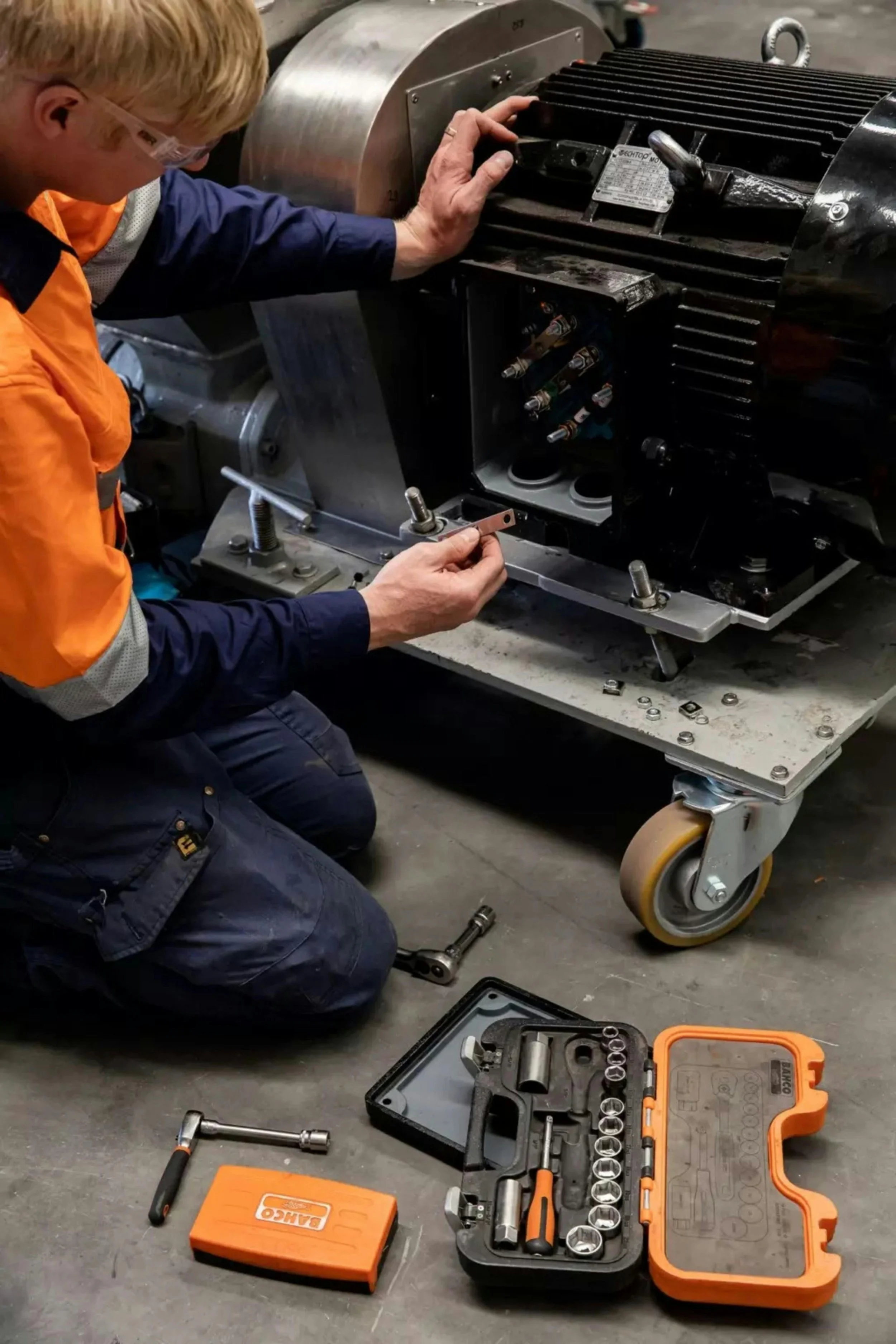 A person working on an electric motor, using tools laid out on the ground, including a socket set and a torque wrench.