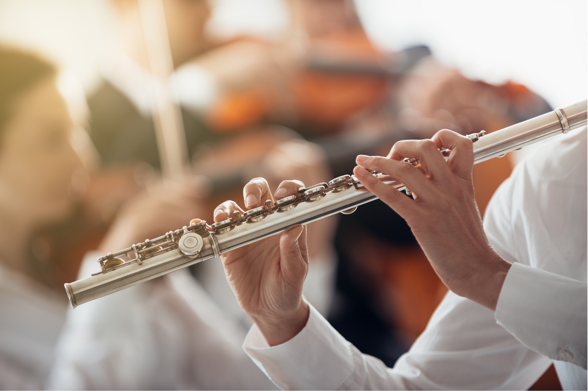 Person playing a silver flute during a performance, focusing on their hands and the instrument.