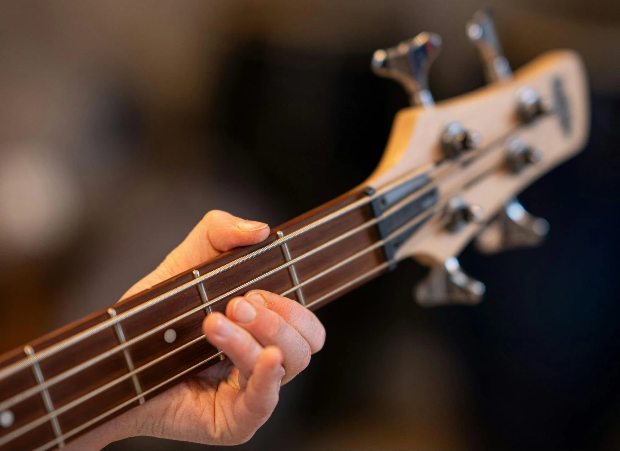 Close-up of a person playing a guitar, focusing on their hand pressing strings on the fretboard.