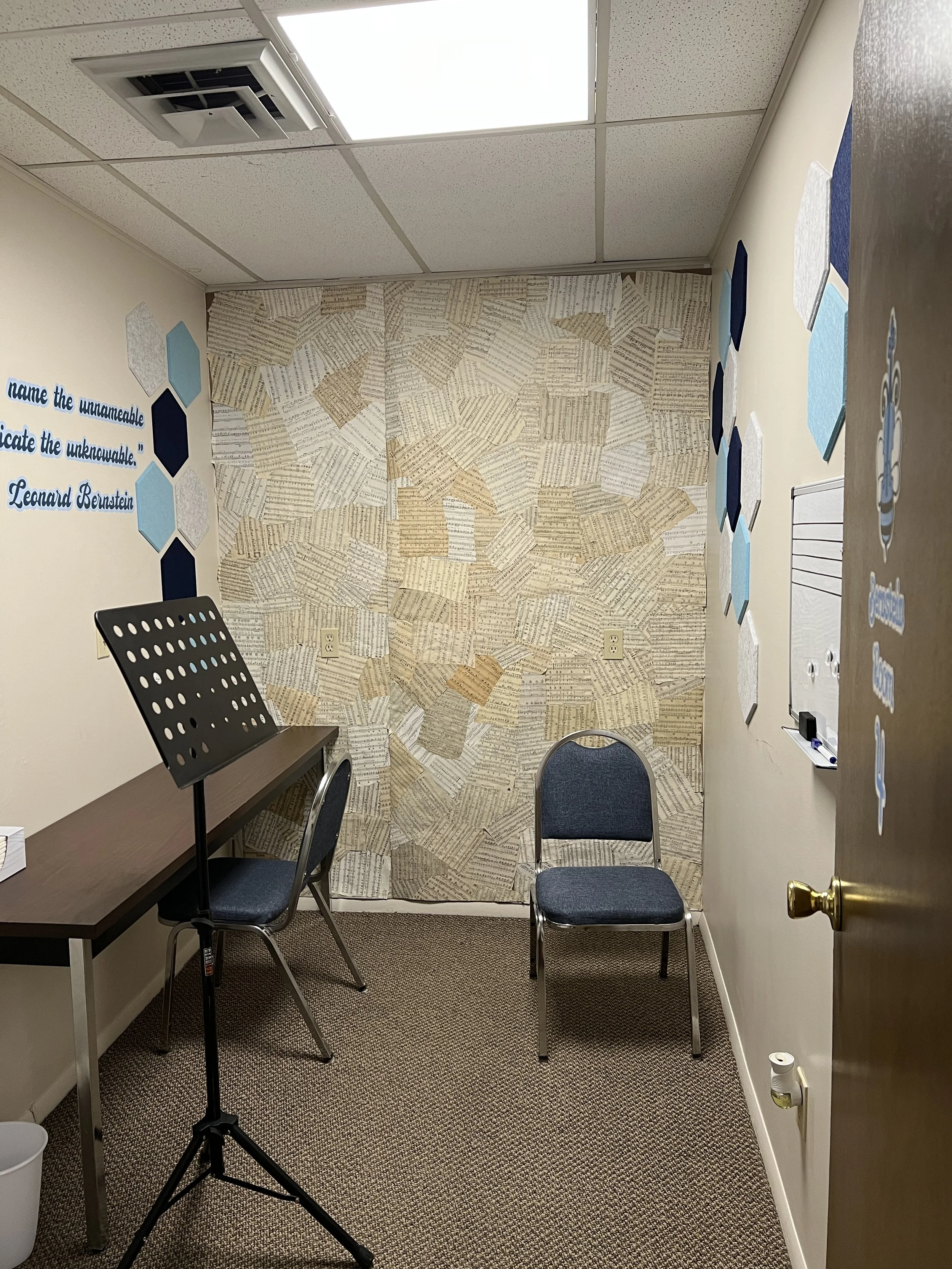 Small room with decorated walls, two chairs, a music stand, and a whiteboard.