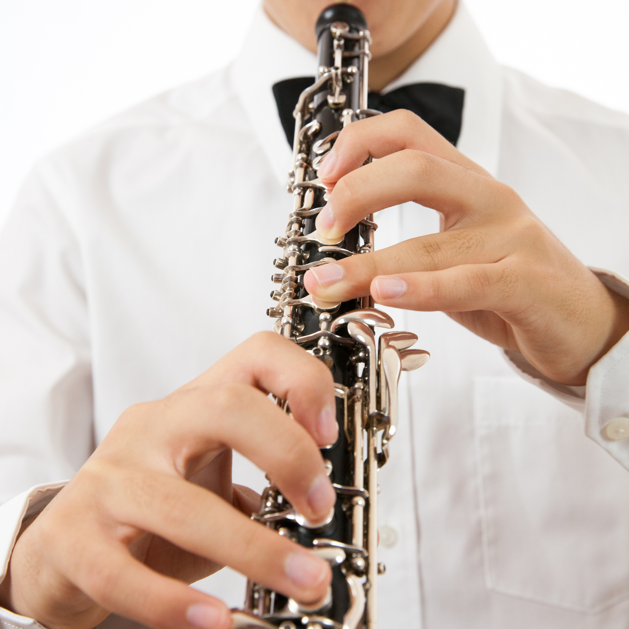 Person playing a clarinet, dressed in a white shirt and black bow tie, holding the instrument with fingers positioned on the keys.