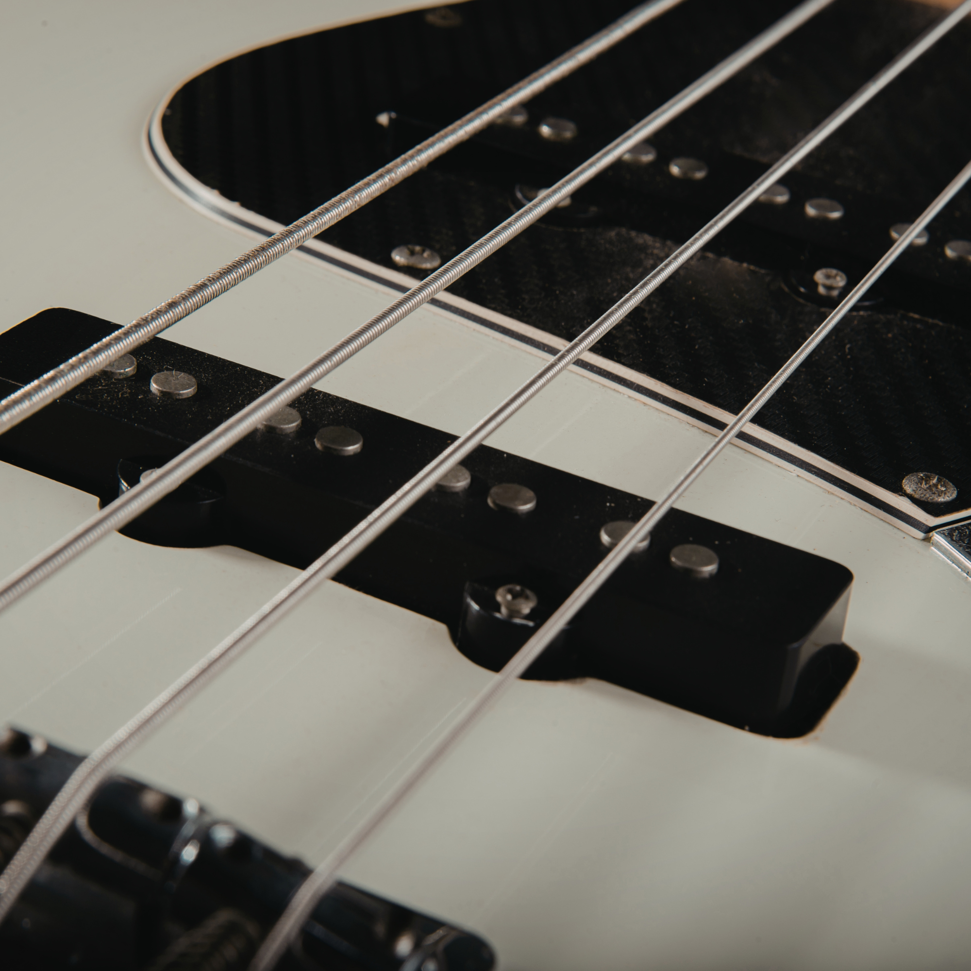Close-up of a guitar's strings, pickups, and body, showing four strings and part of the pickups.