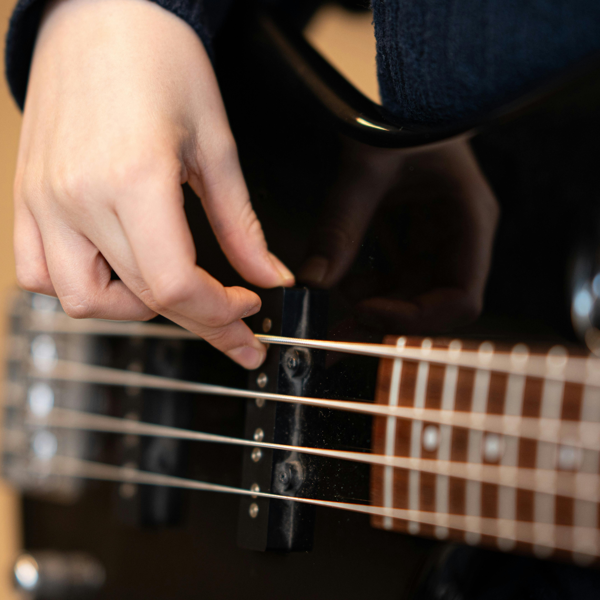 Close-up of a person's hand adjusting the bridge of an electric guitar.