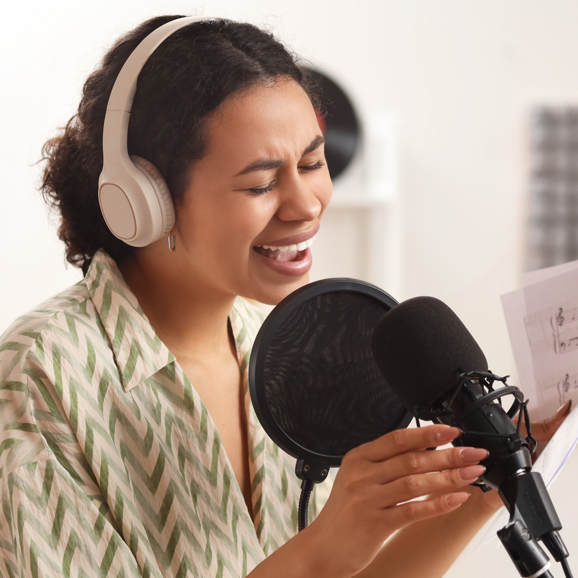 woman singing into a microphone with headphones, holding music sheets.