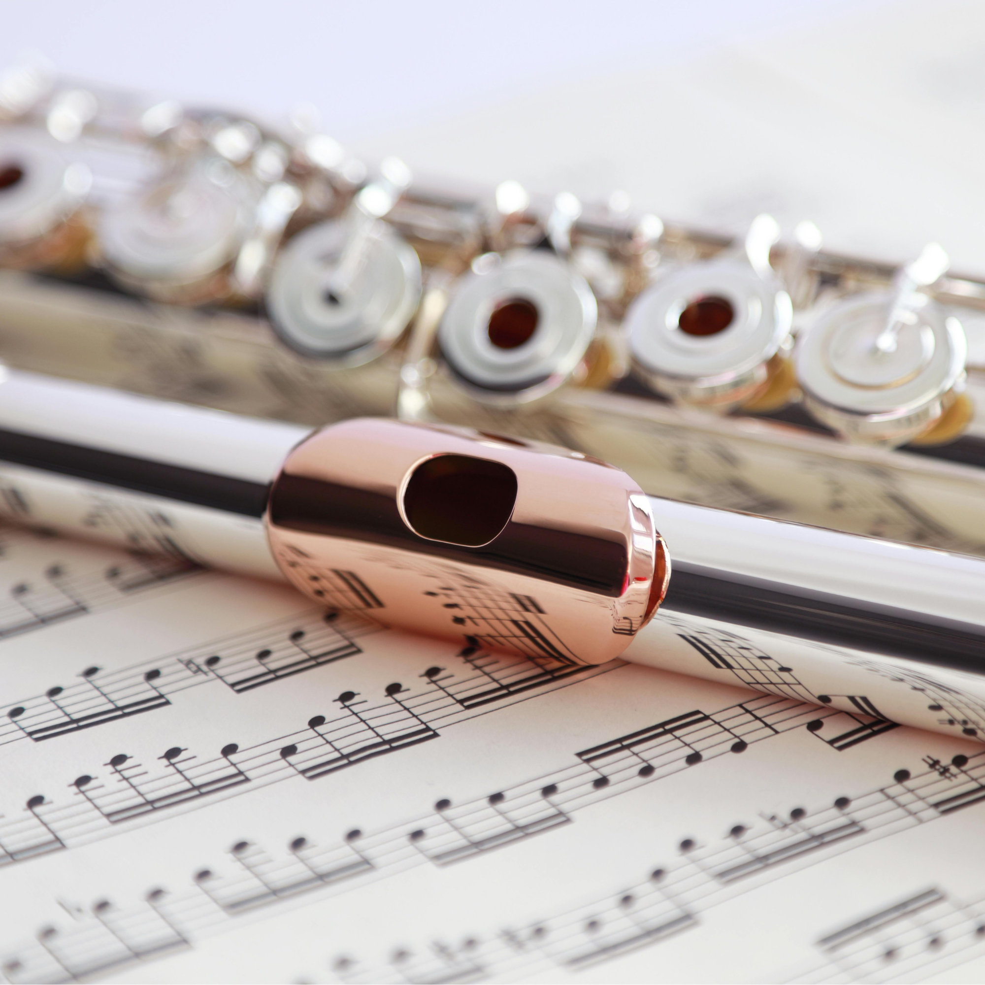 Close-up of a silver flute, a rose gold harmon mute, and sheet music.