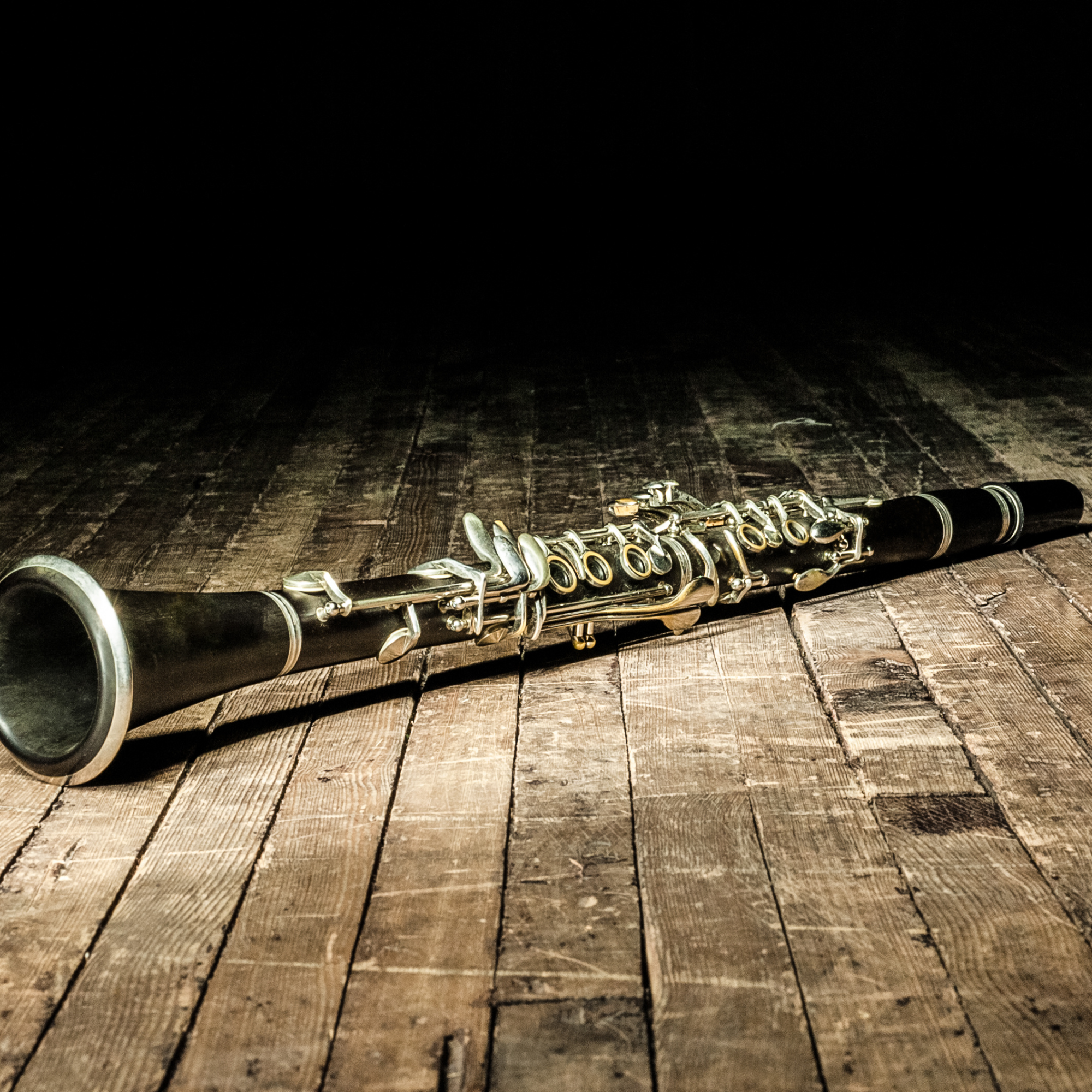 A black soprano saxophone lying on a wooden floor in a dimly lit room.