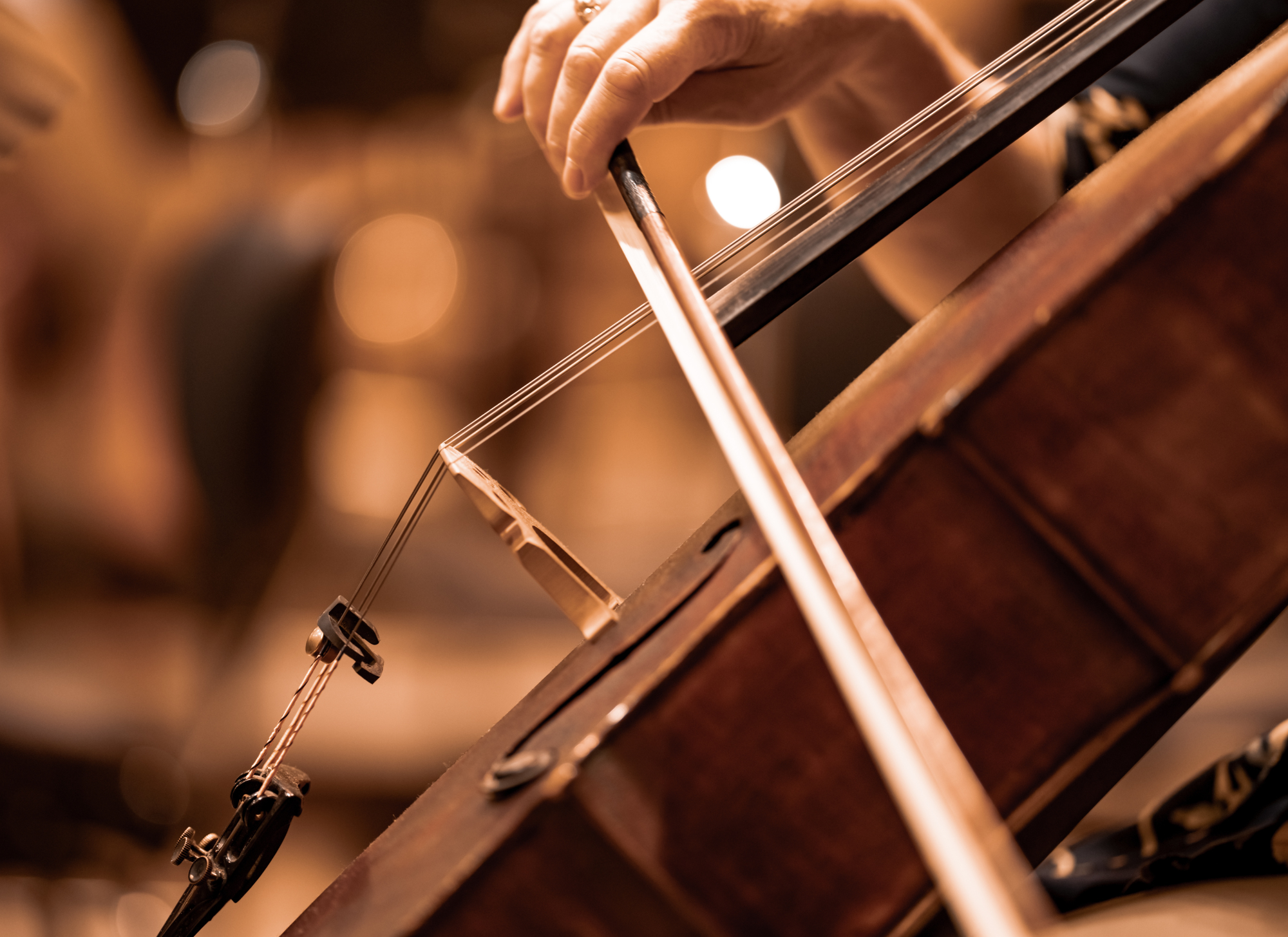 Close-up of a person's hand playing a vintage wooden violin, focusing on the hand, the bow, and the strings.