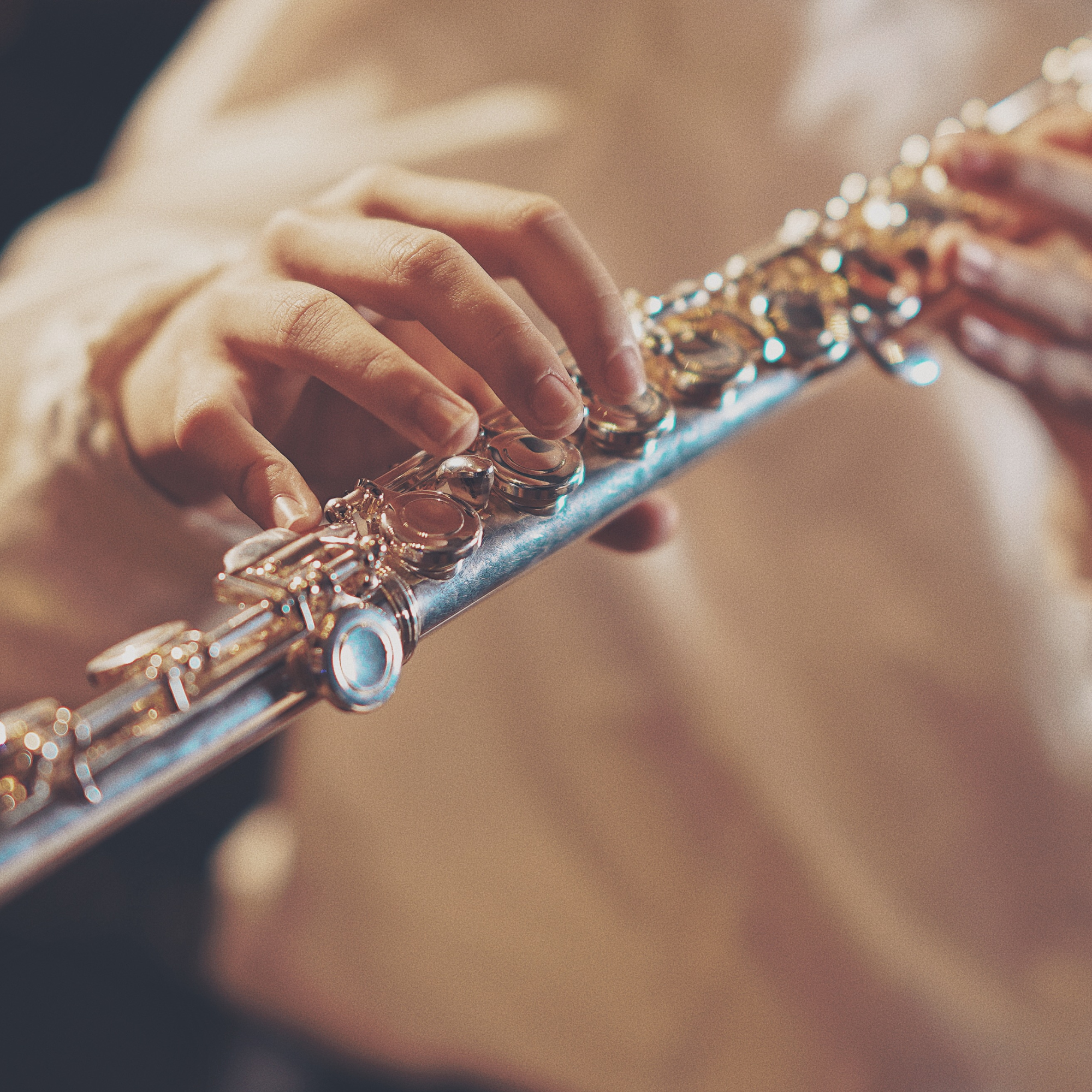 A person playing a silver flute, focusing on their fingers pressing the instrument's keys.