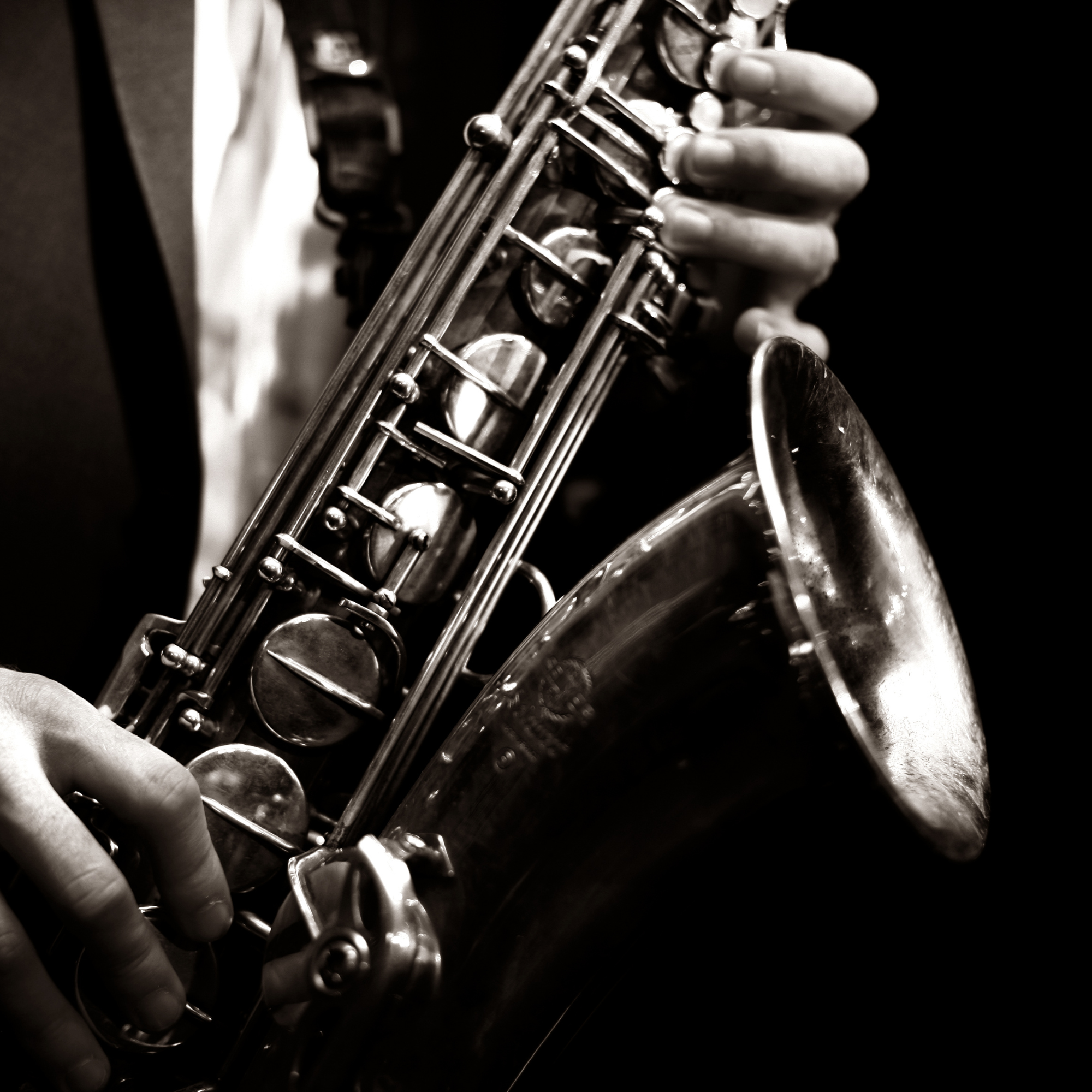 Close-up of a person playing a saxophone, focusing on their hand and the instrument in black and white.