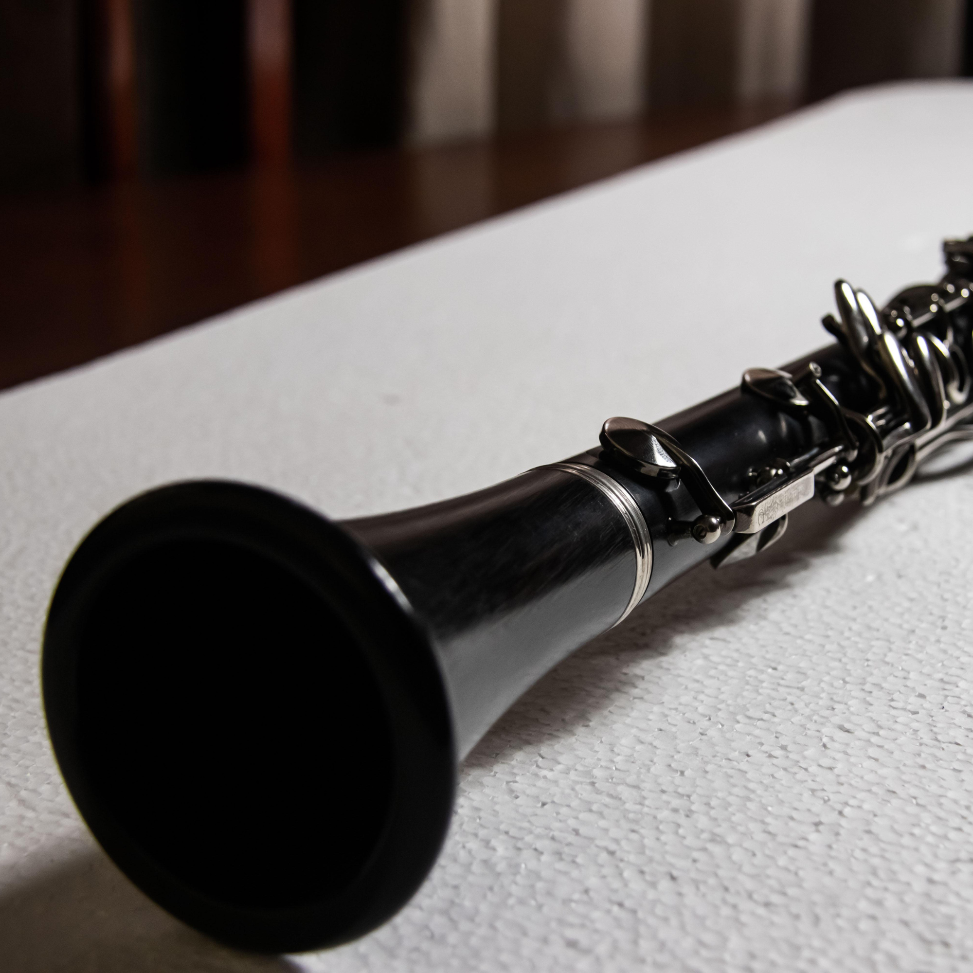 Close-up of a black clarinet lying on a white textured surface.